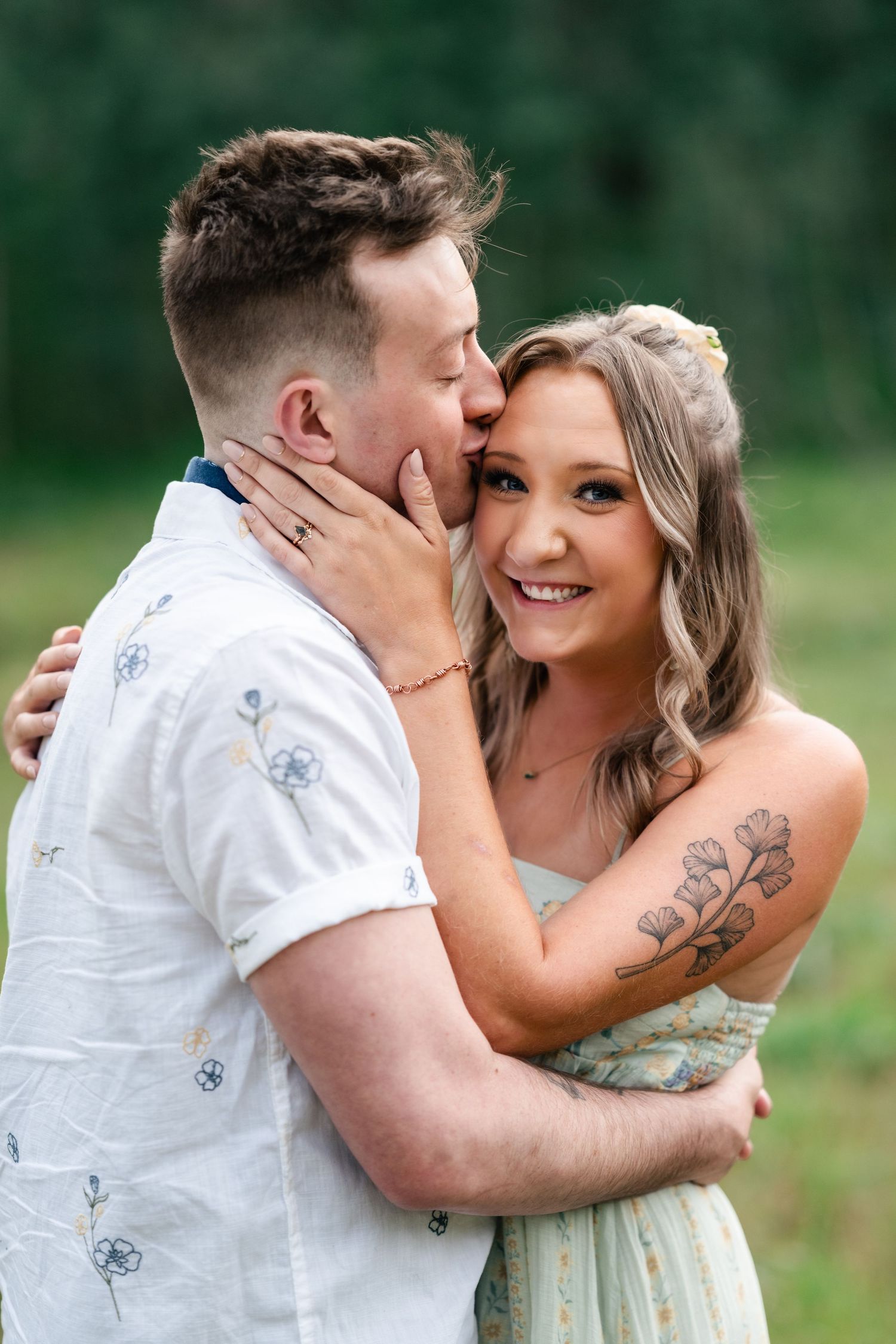 A tender moment captured between a couple embracing in a lush green outdoor setting.