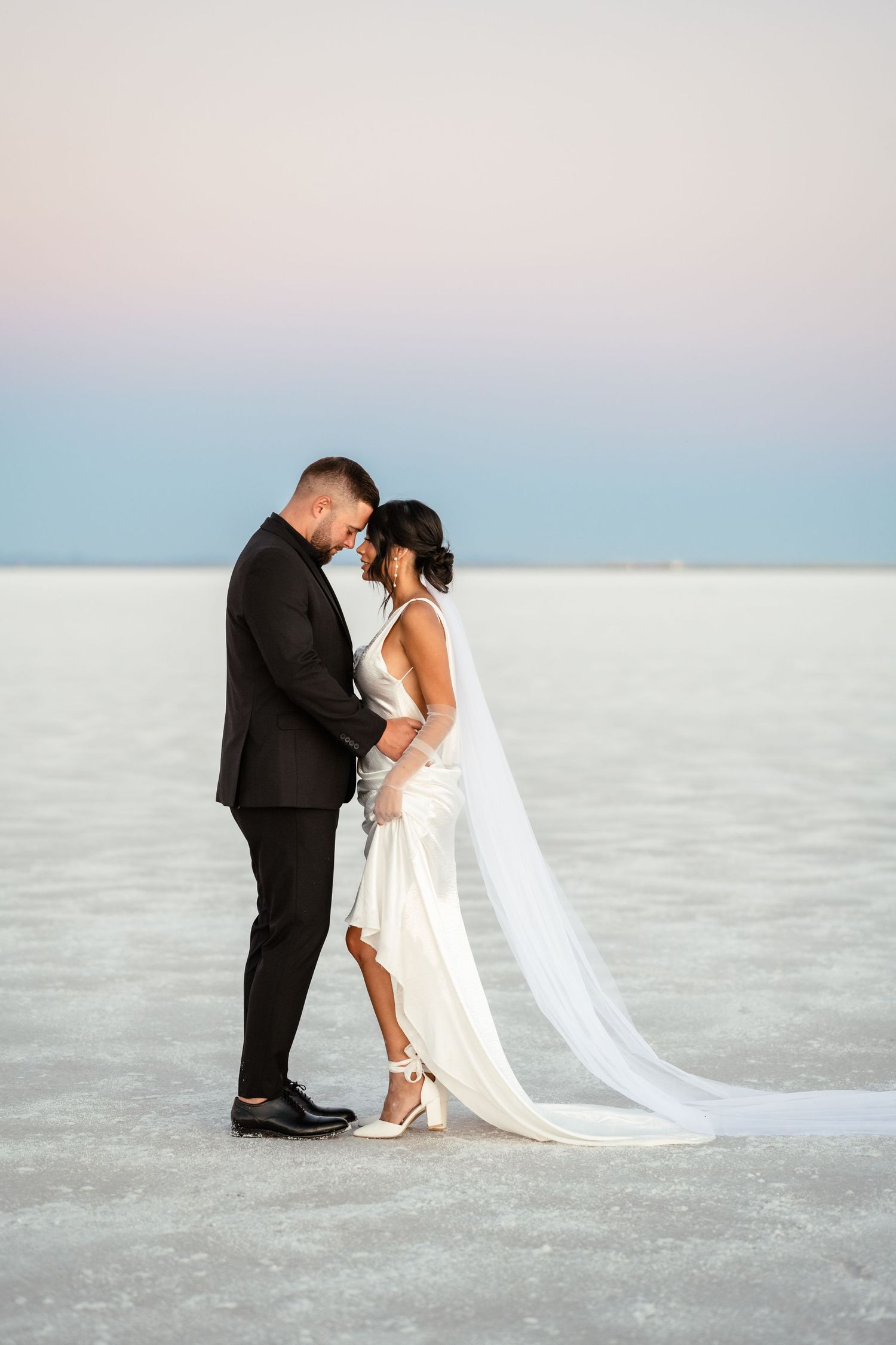 Intimate wedding couple portraits on salt flats with soft pastel sky in background.