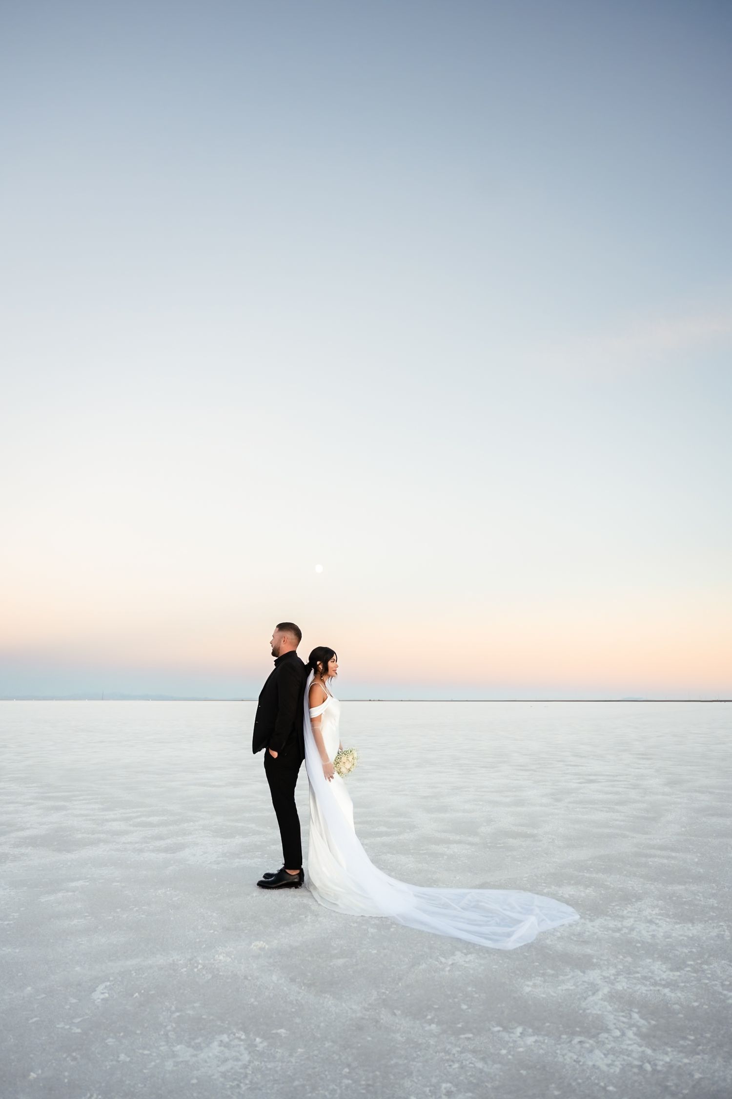 Wedding couple walks across expansive salt flats during sunset photoshoot.