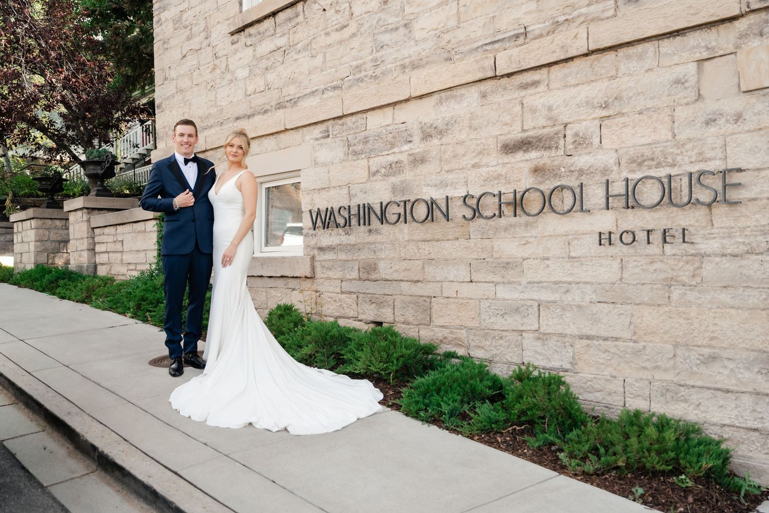A wedding couple poses on stone steps outside the historic Mansion School House Hotel.