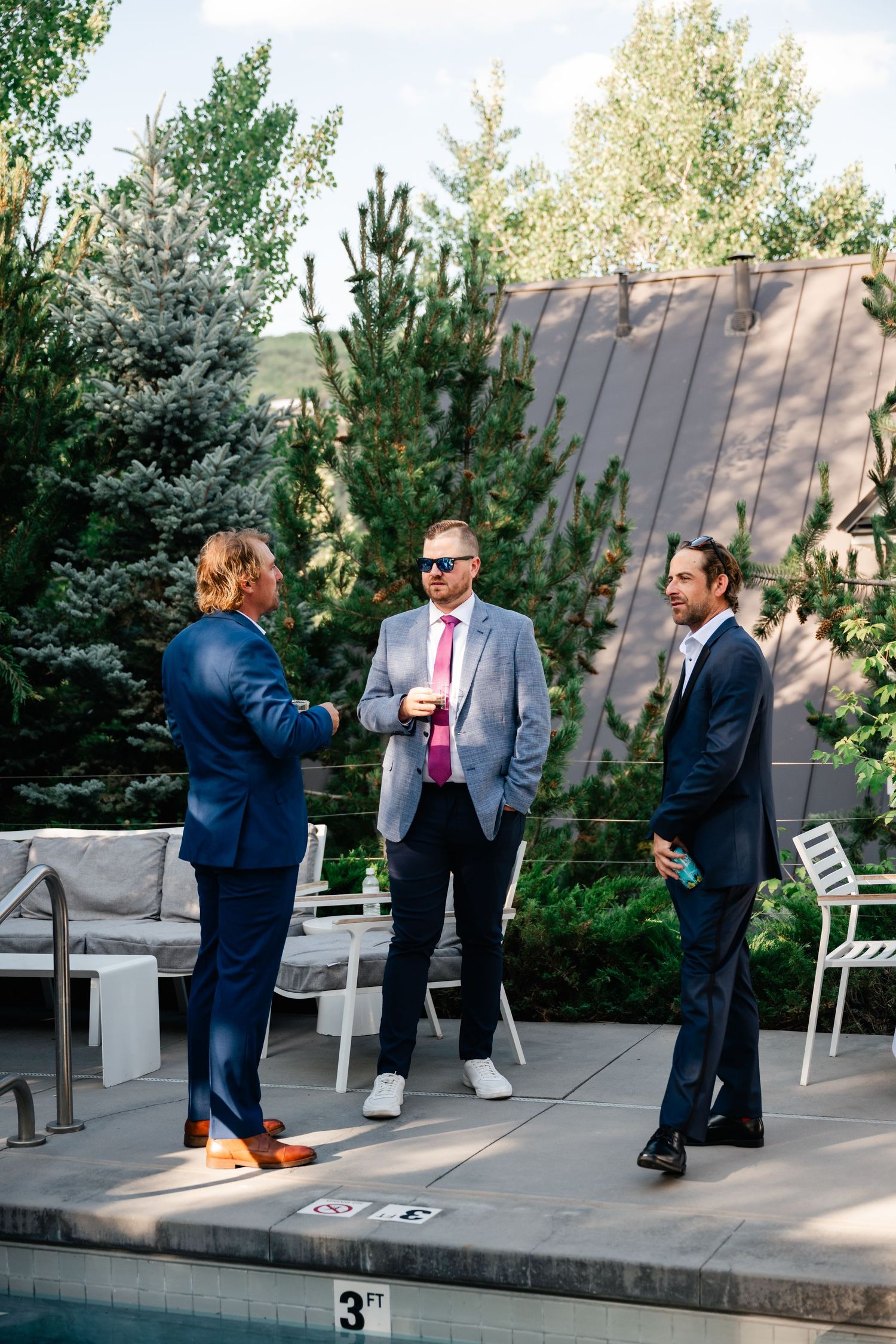 Wedding party members in formal attire socialize on an outdoor patio.