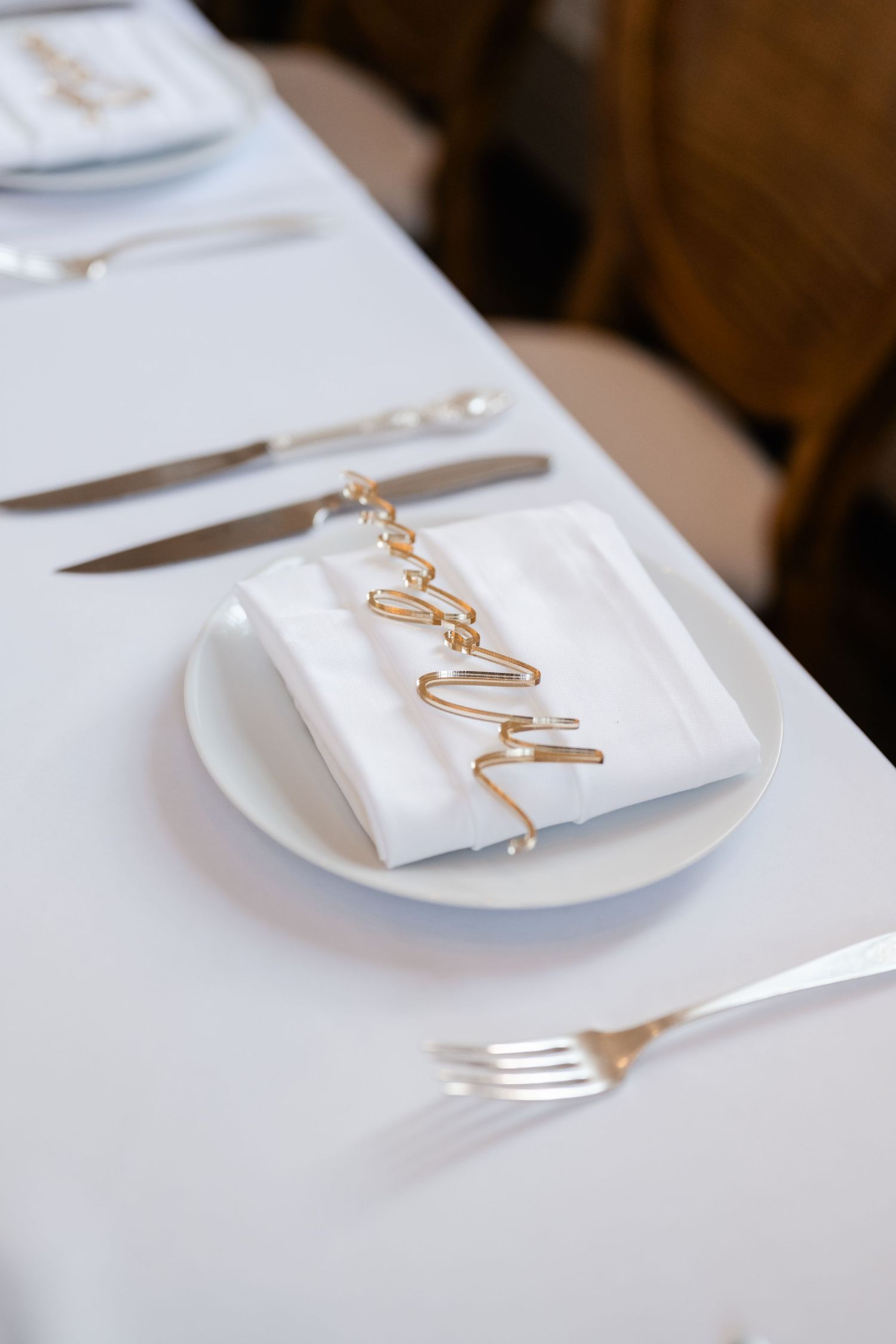 Place settings feature elegant white napkins with gold decorative elements on white tablecloths.
