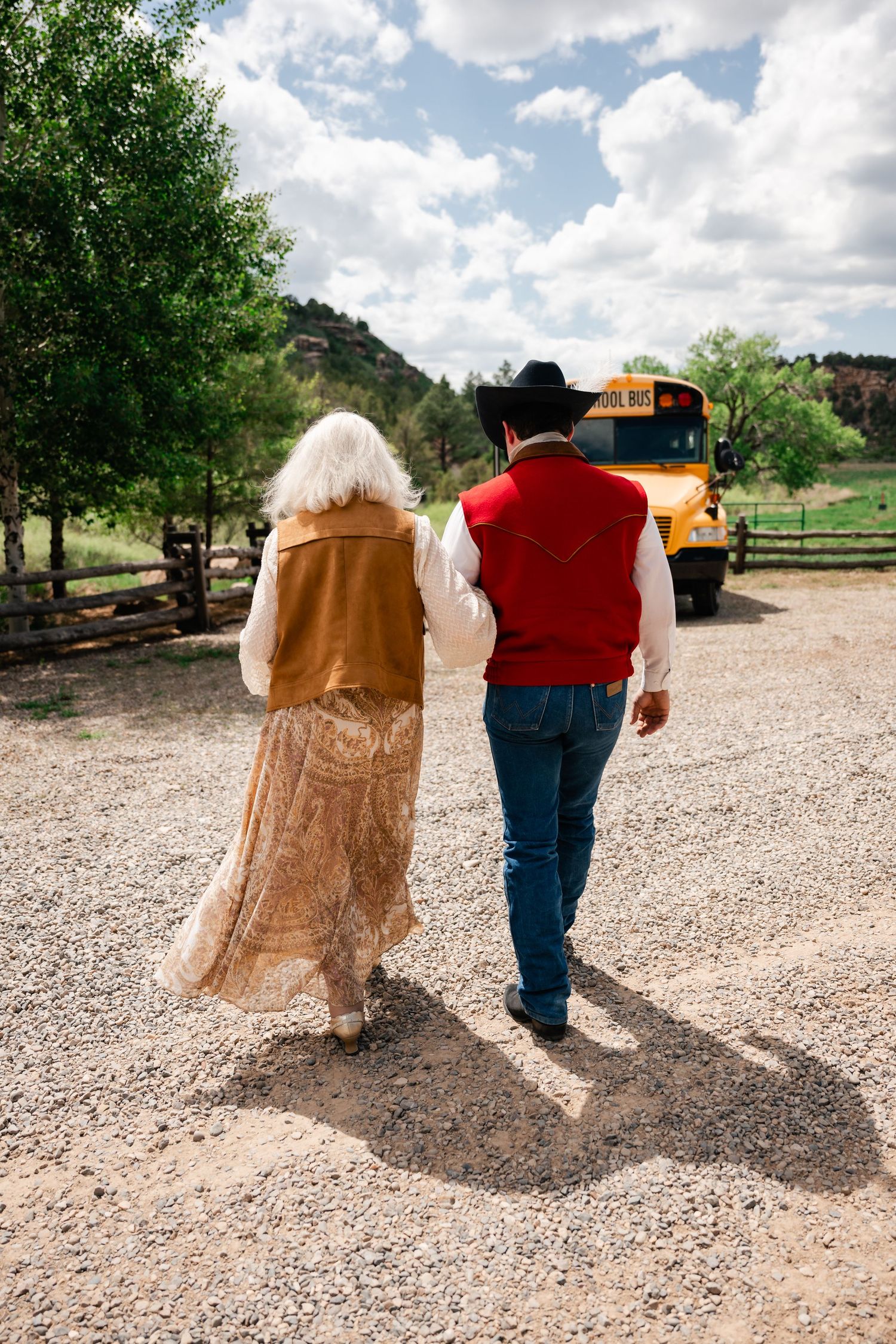 Two people walking together on a gravel path wearing western-style formal attire.