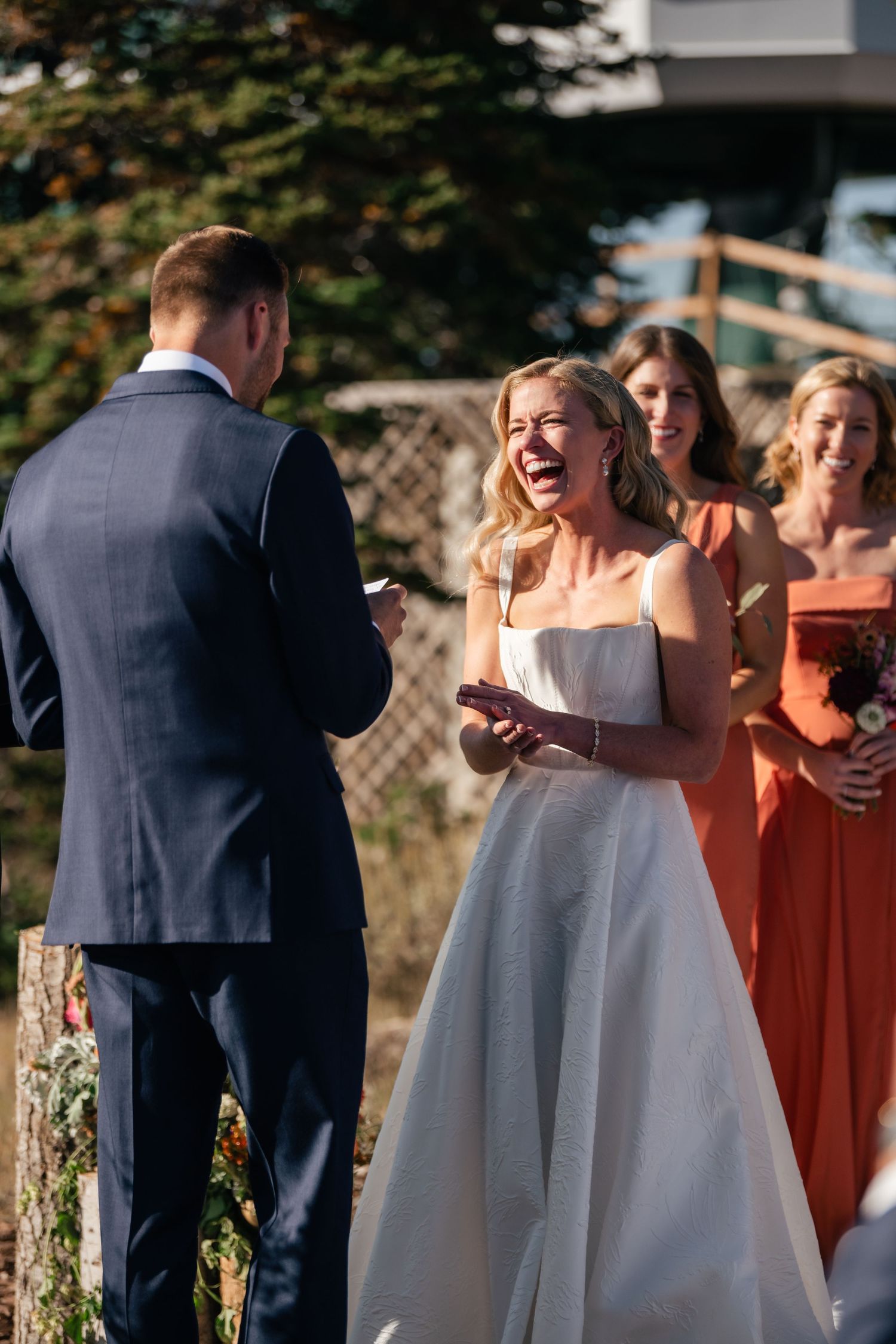 Wedding party gathered outdoors with bridesmaids in coral dresses.