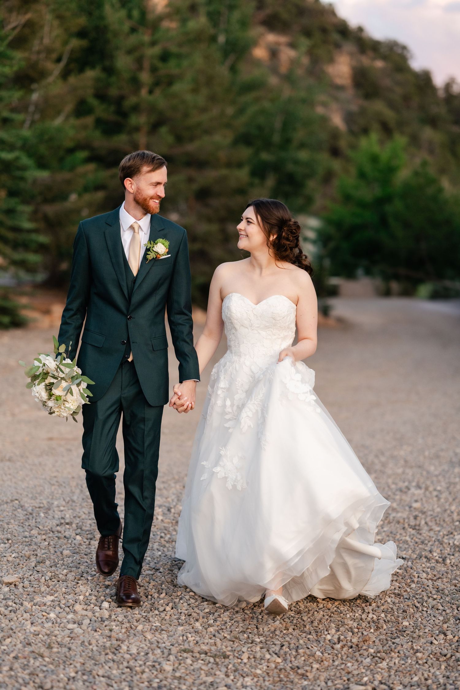 Couple walking hand in hand on gravel path surrounded by natural landscape.