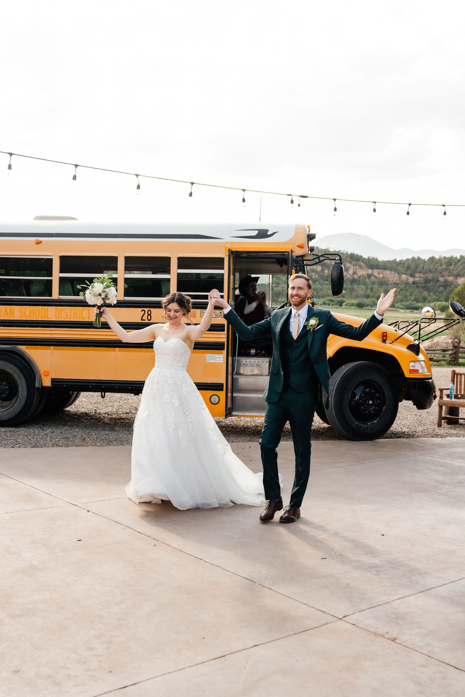 Newlywed couple poses playfully in front of a yellow school bus on their wedding day.