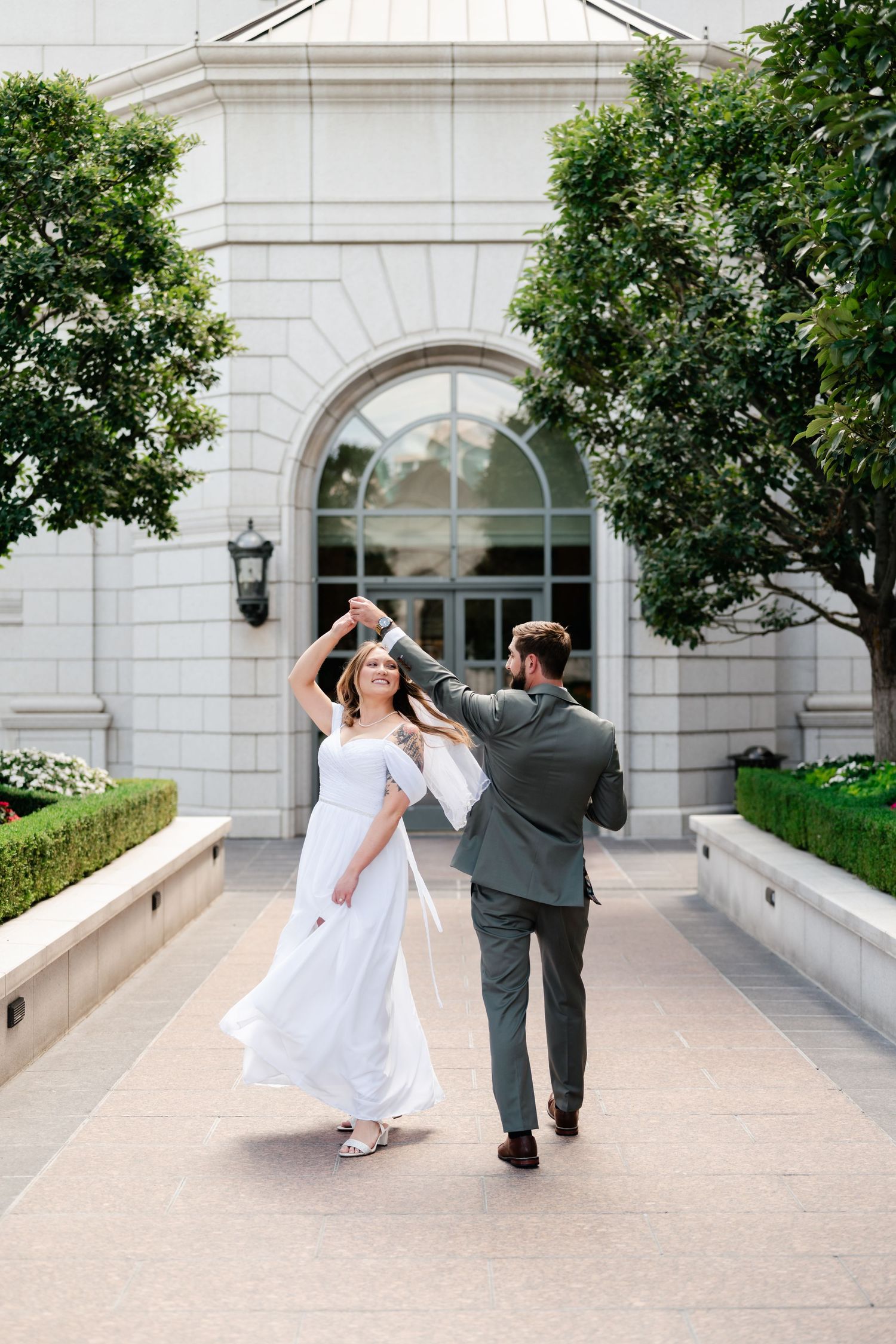 A bride and groom dance playfully on an outdoor plaza with classical architecture in the background.