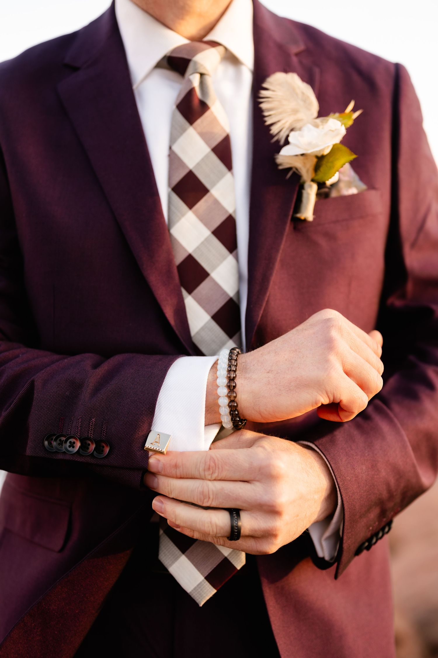 Close-up details of a burgundy suit with checkered tie and boutonniere.