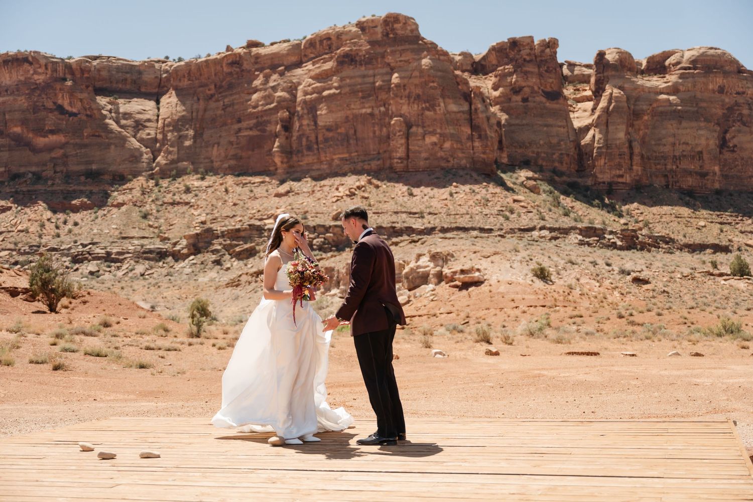 Couple exchanging vows at desert wedding ceremony with stunning red rock canyon backdrop in arid landscape.