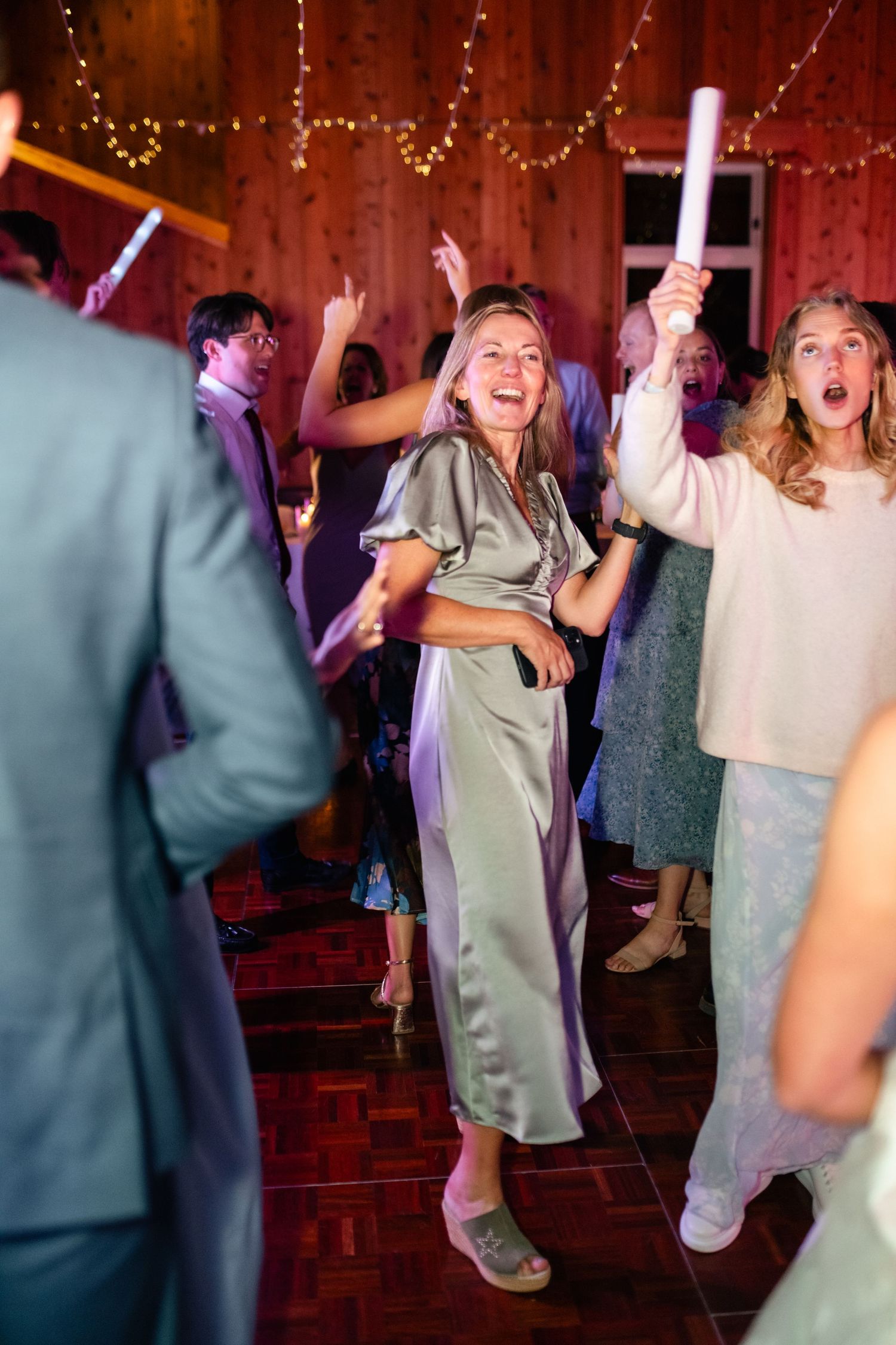 Wedding reception guests dancing and celebrating in a rustic barn venue decorated with string lights.