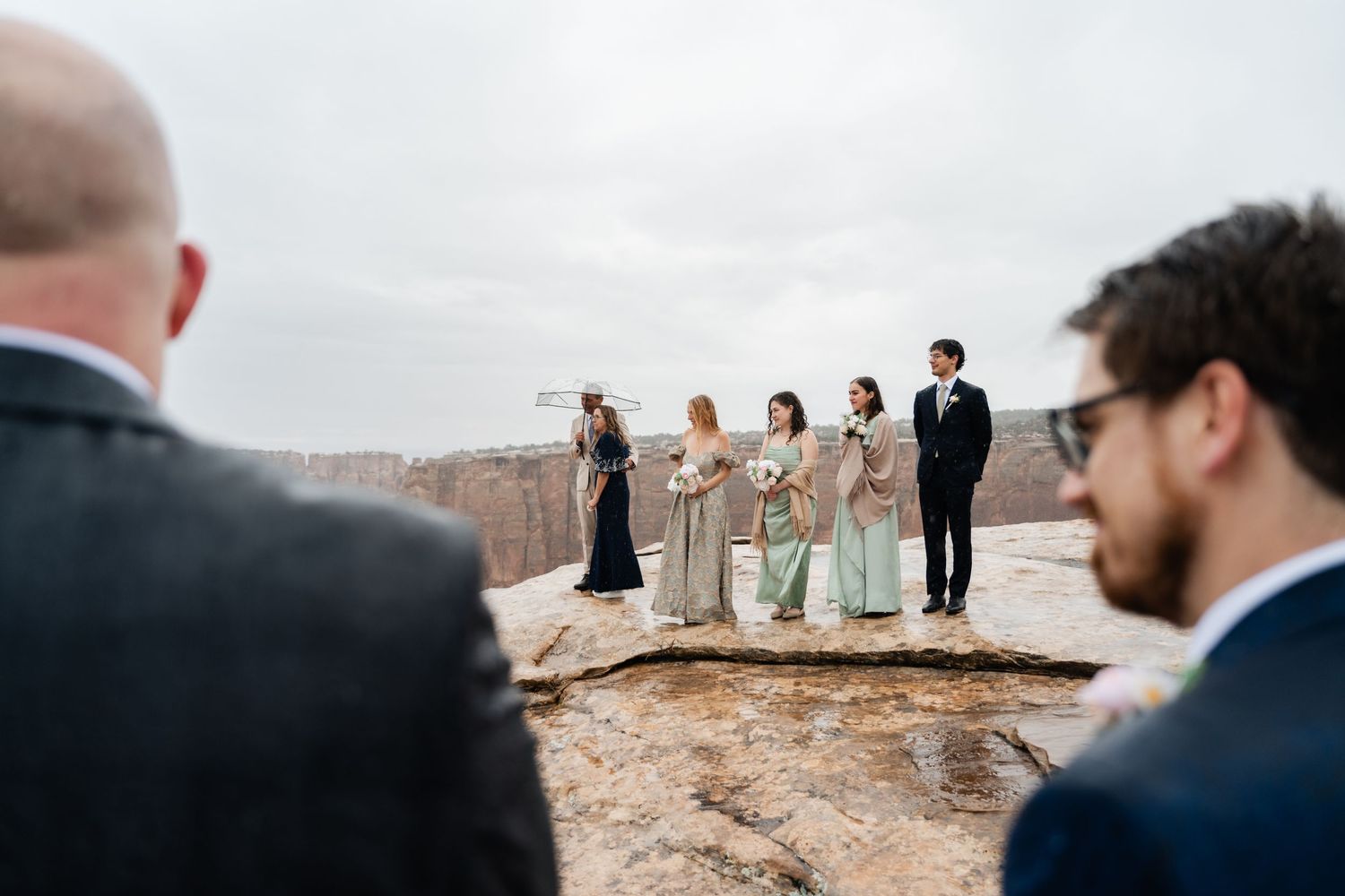Wide angle shot of wedding party gathered on scenic desert overlook for photographs.