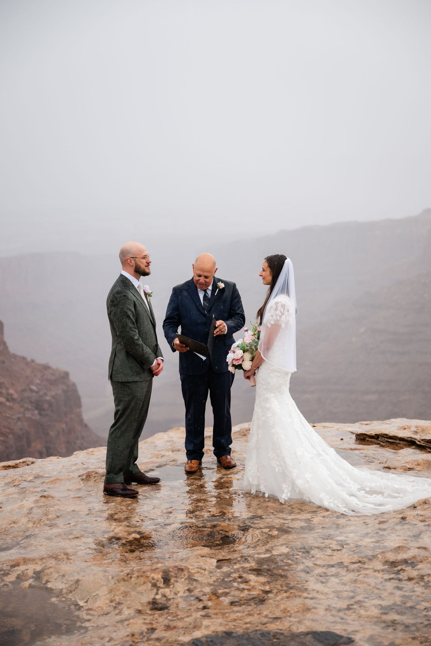 Wedding ceremony taking place on dramatic cliffside overlook with officiant and couple in formal attire.