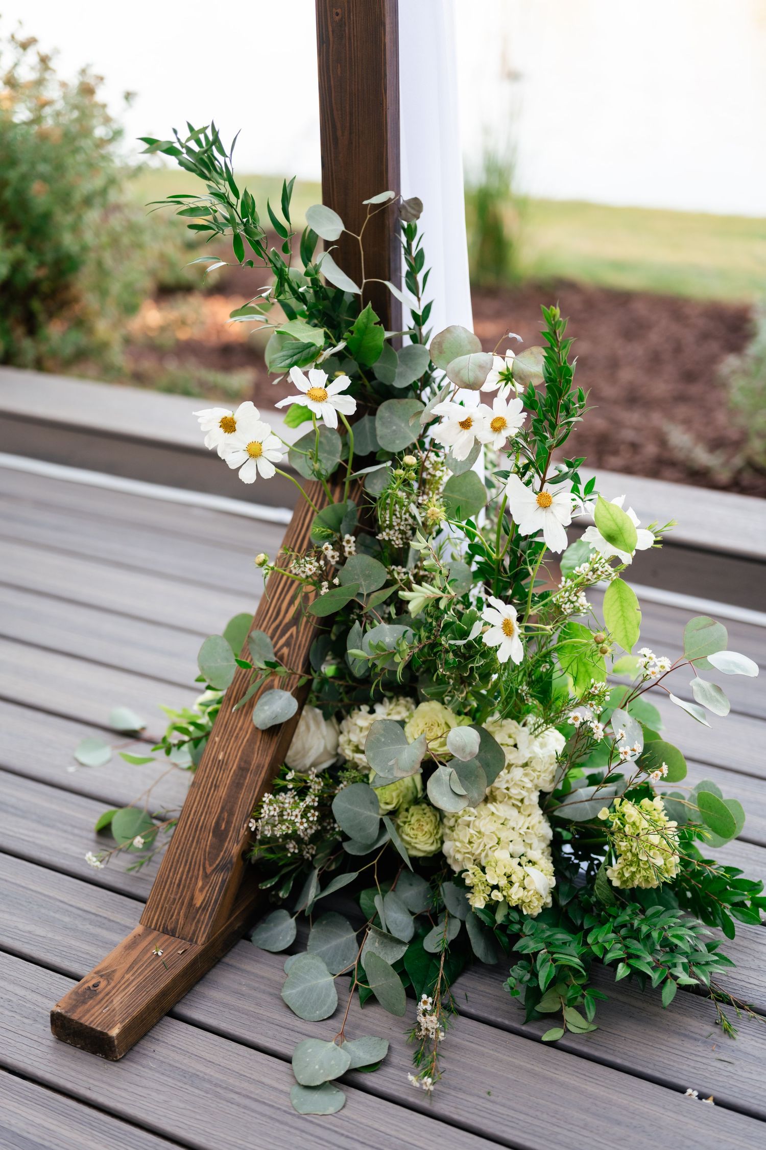 Elegant floral arrangement with white flowers and greenery cascading down wooden stairs on a deck.