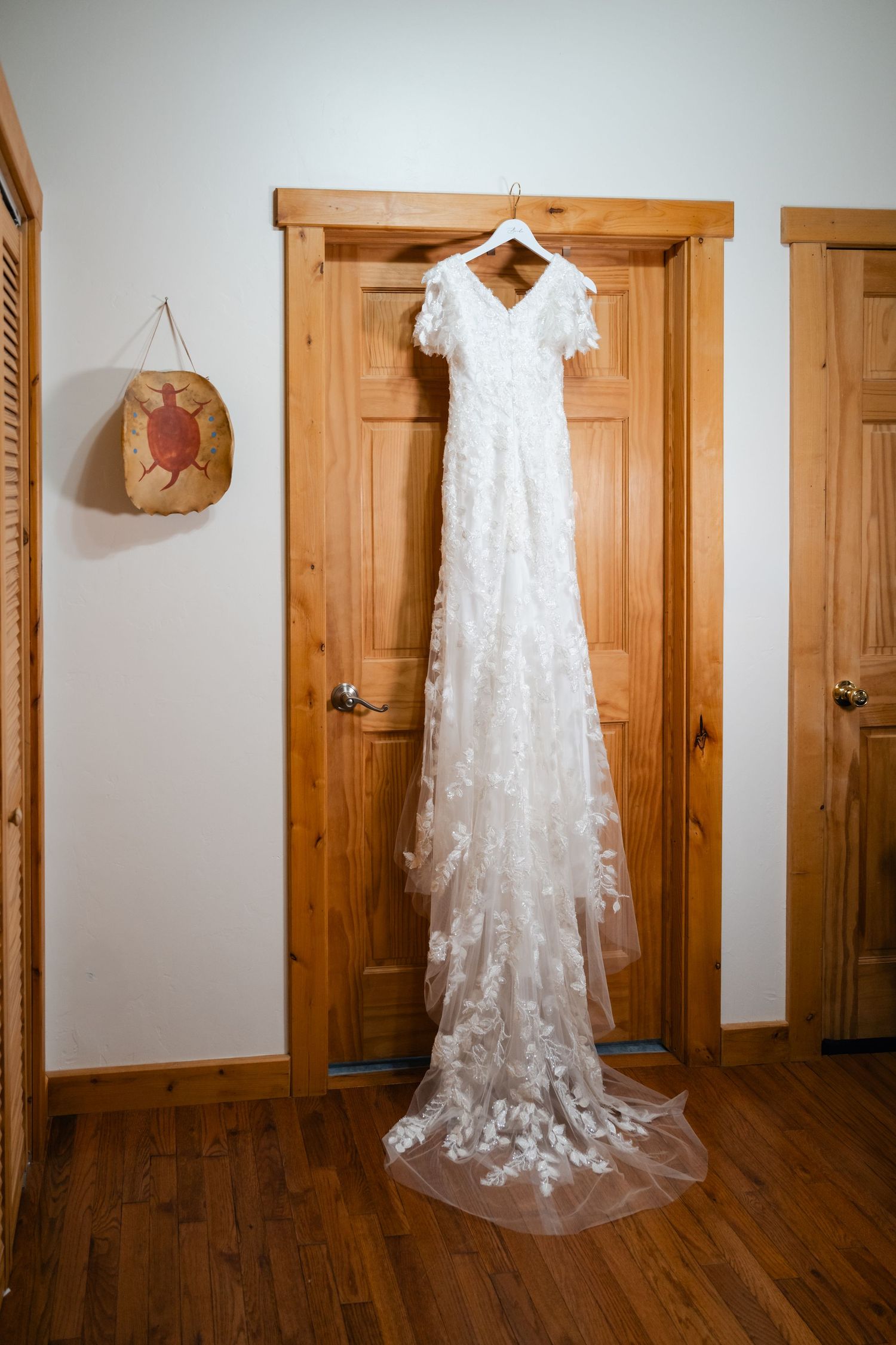 A white lace wedding dress hangs elegantly against wooden doors in a rustic interior setting.