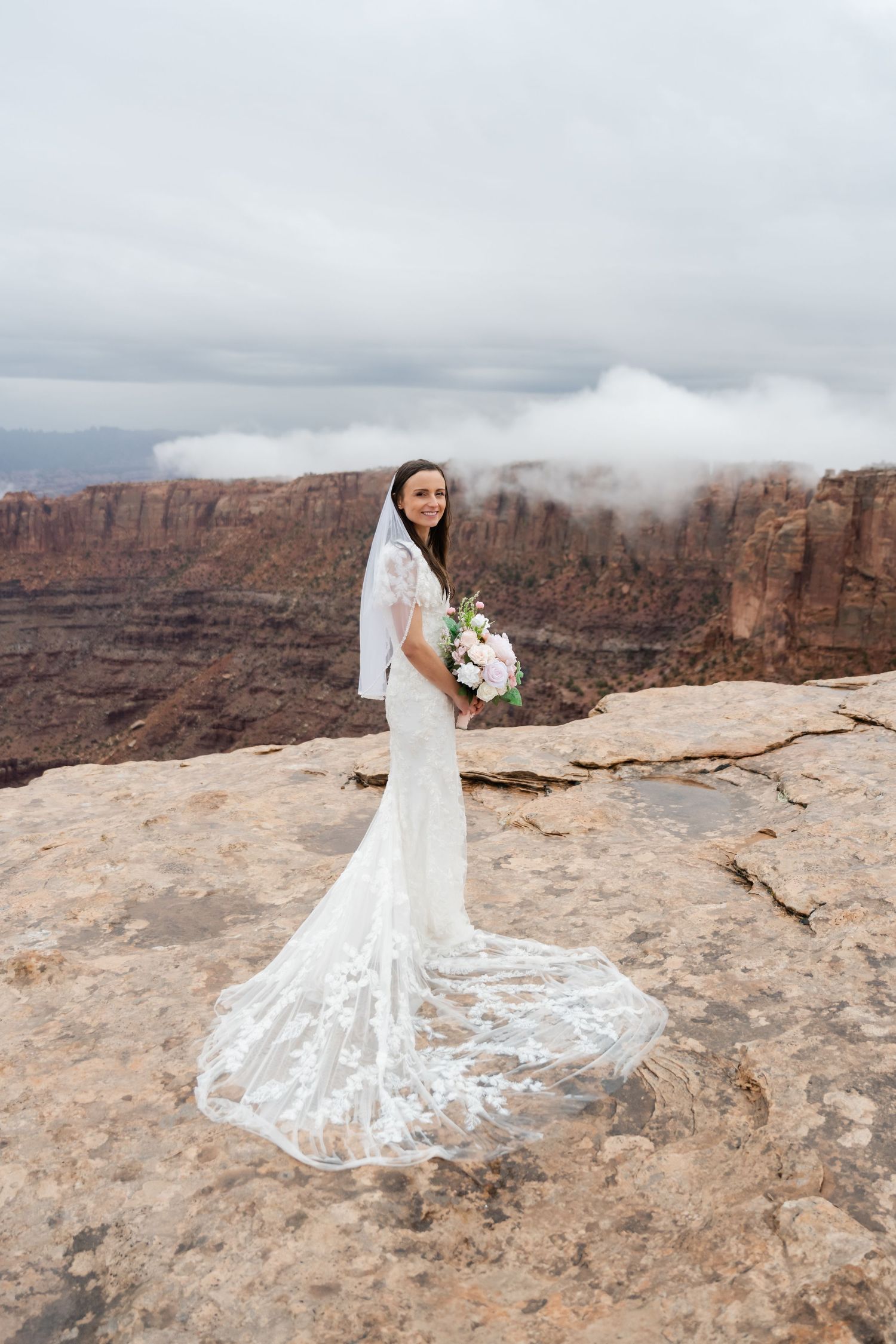 A bride's lace dress train flows beautifully against red rock canyon views.