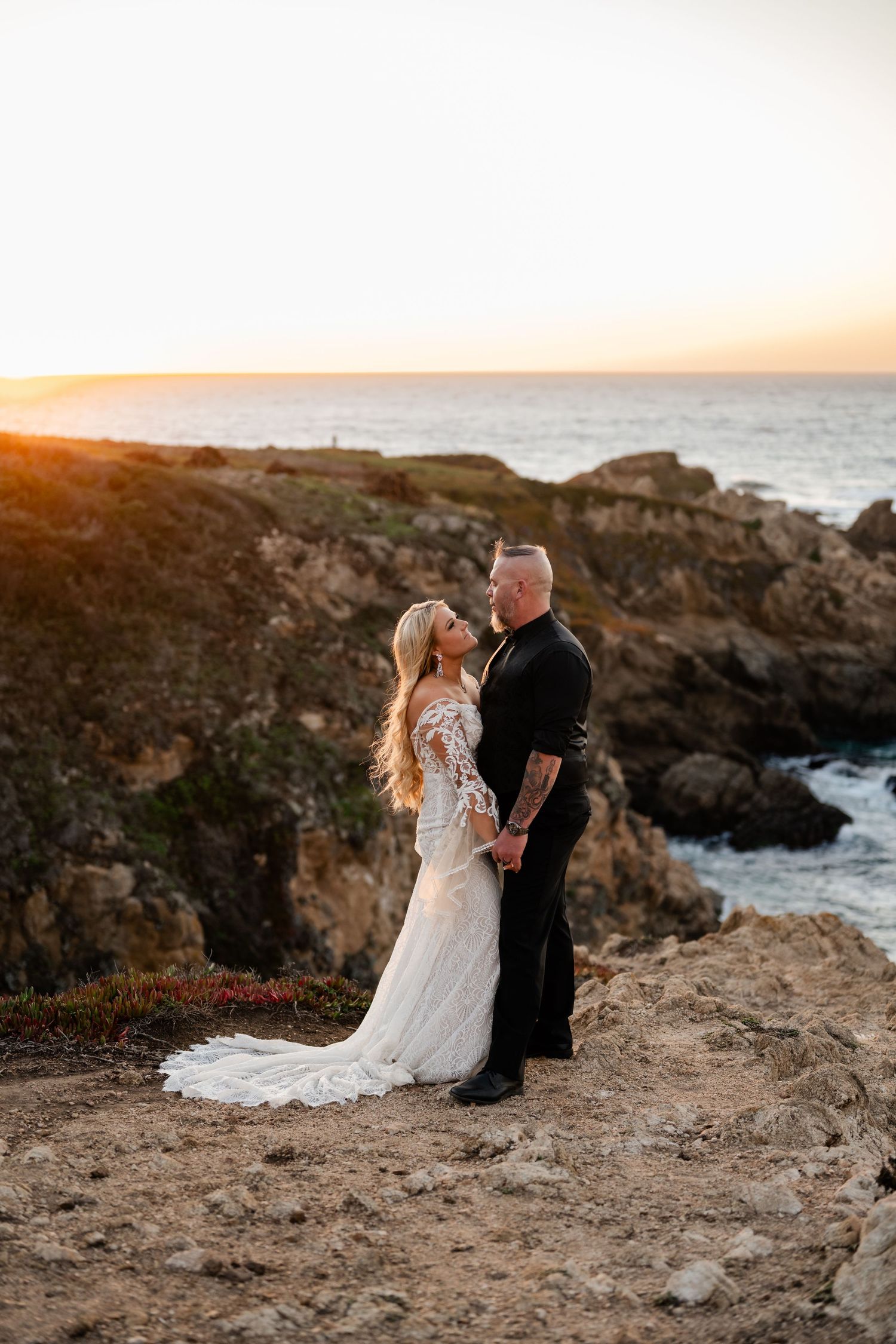 A romantic coastal wedding photo during golden hour with dramatic cliffs and ocean views.