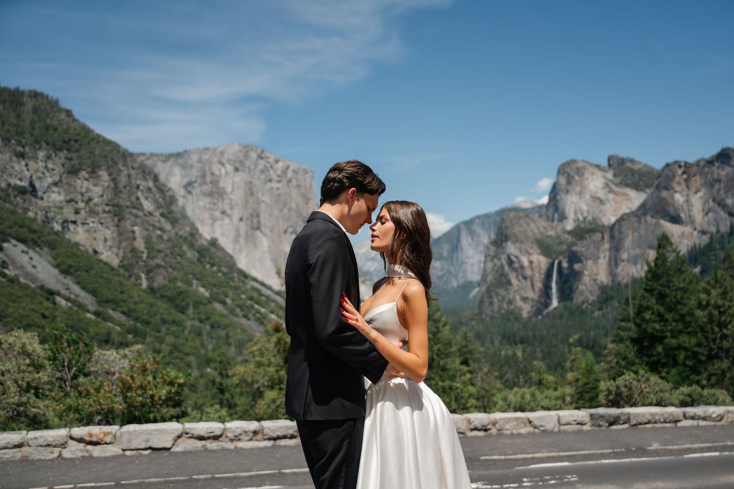 Couple shares romantic moment at Yosemite Valley with Bridalveil Fall and granite cliffs backdrop on wedding day.