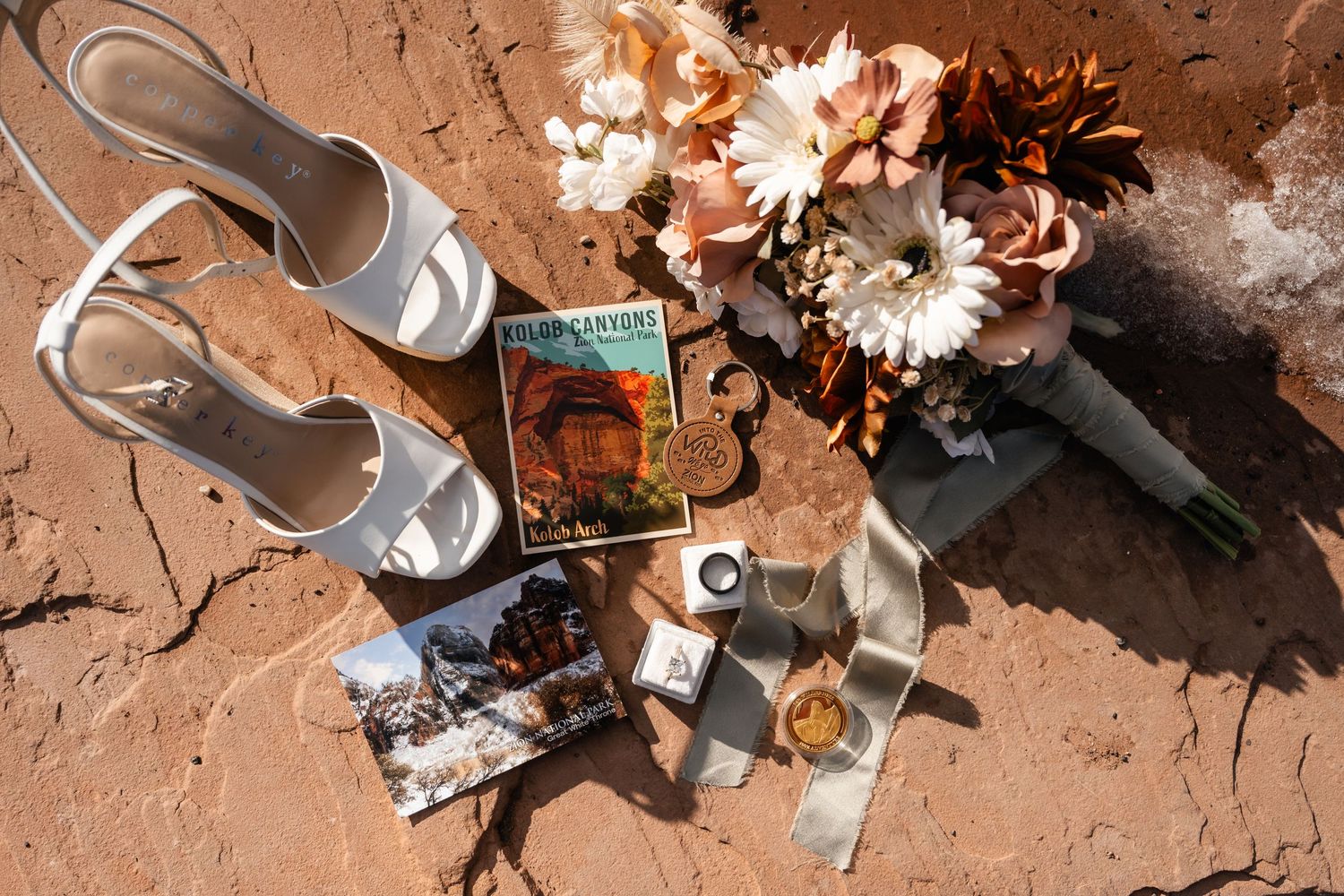 Wedding details including shoes, flowers and decorative items arranged on red desert rock.