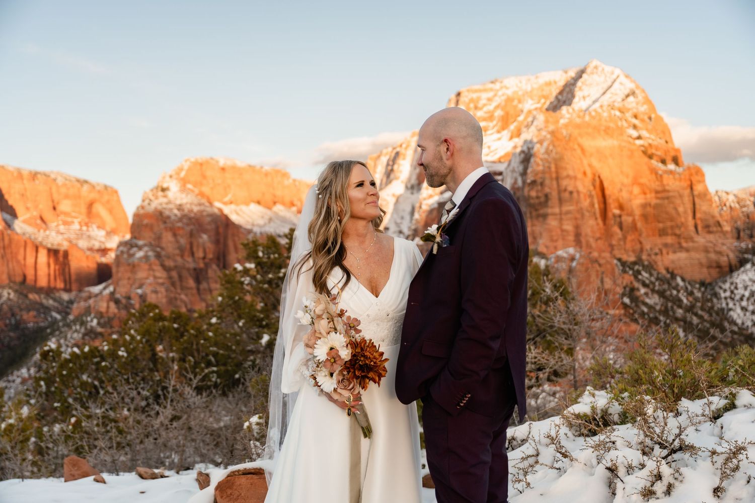 Romantic winter wedding portraits with snow-covered red rocks and mountains in the background.