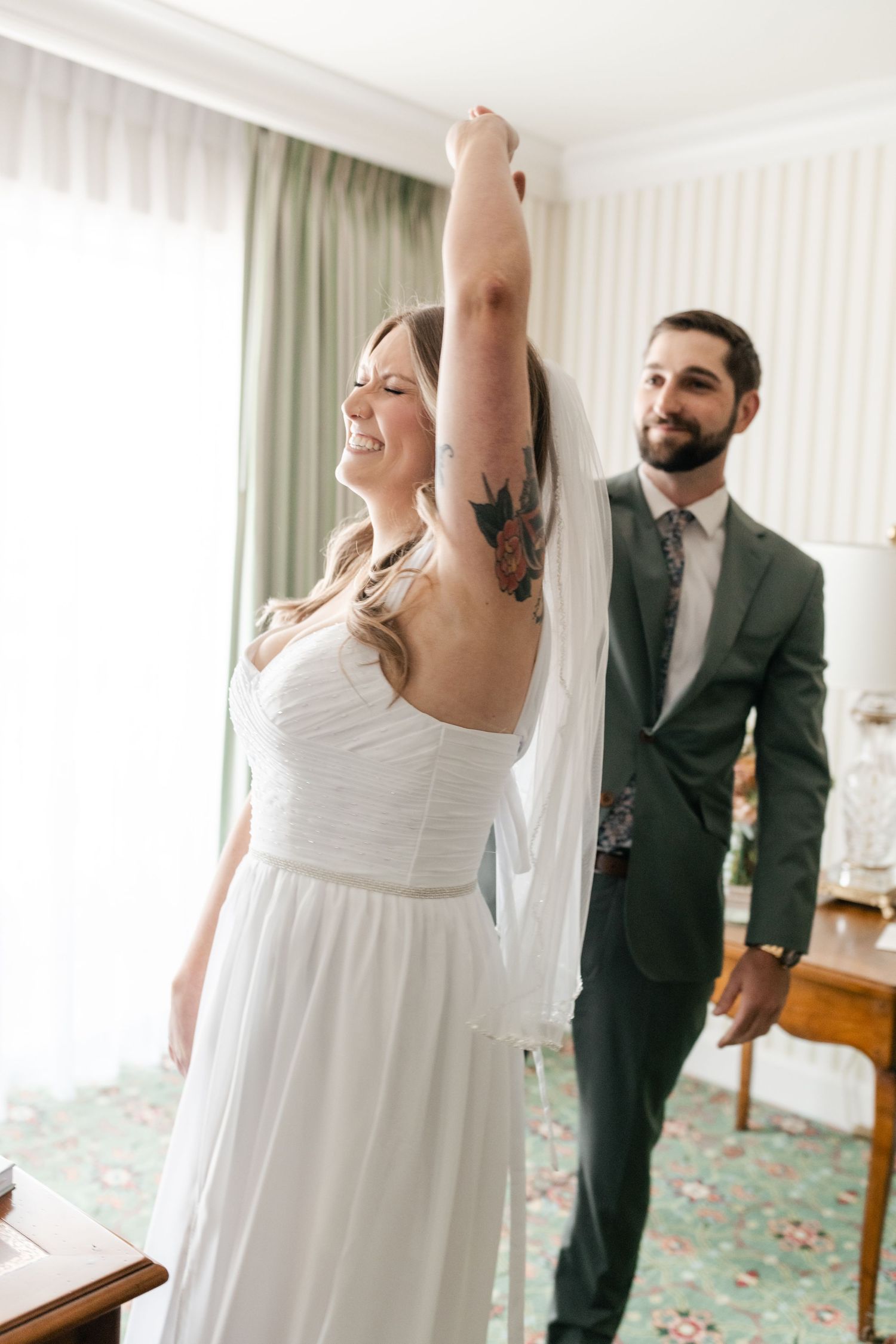 A joyful wedding first look reaction in a bright hotel room with vintage decor.