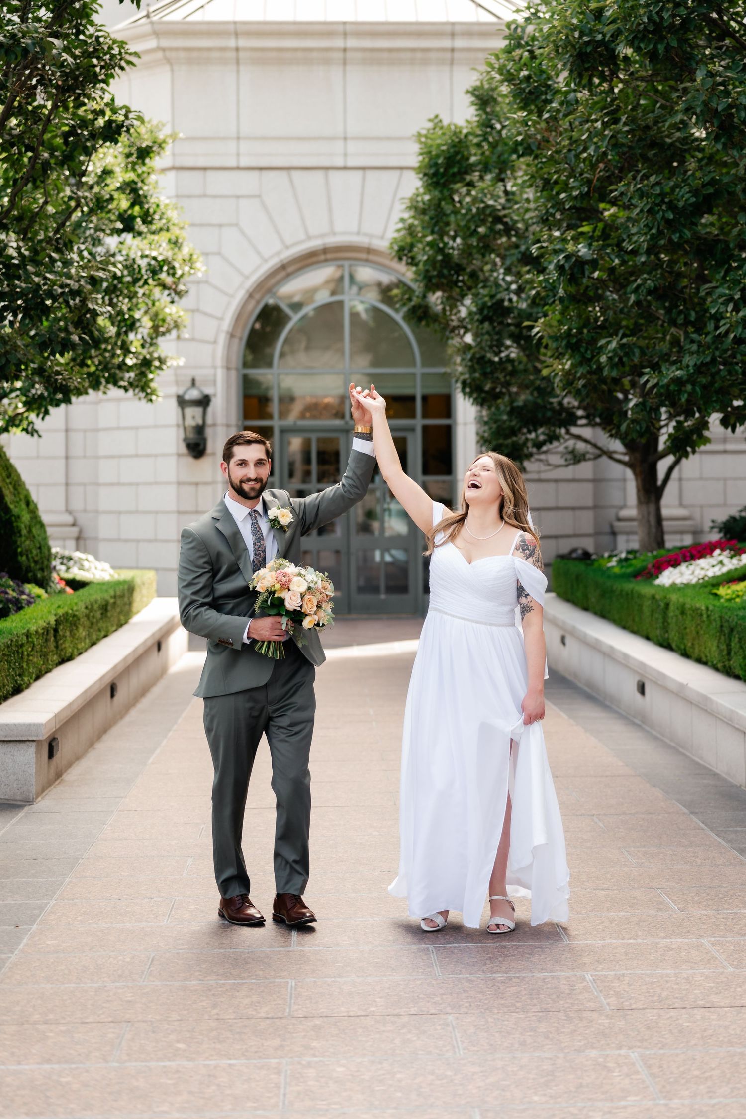 A couple celebrates their wedding day with joyful dancing on a stone pathway surrounded by trees.