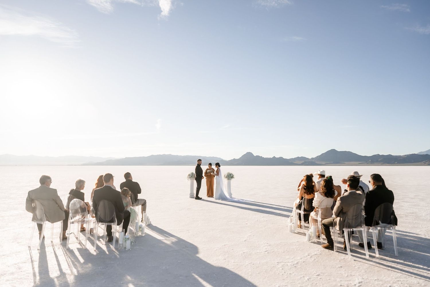 Wedding party silhouettes against bright white salt flats and mountain backdrop.