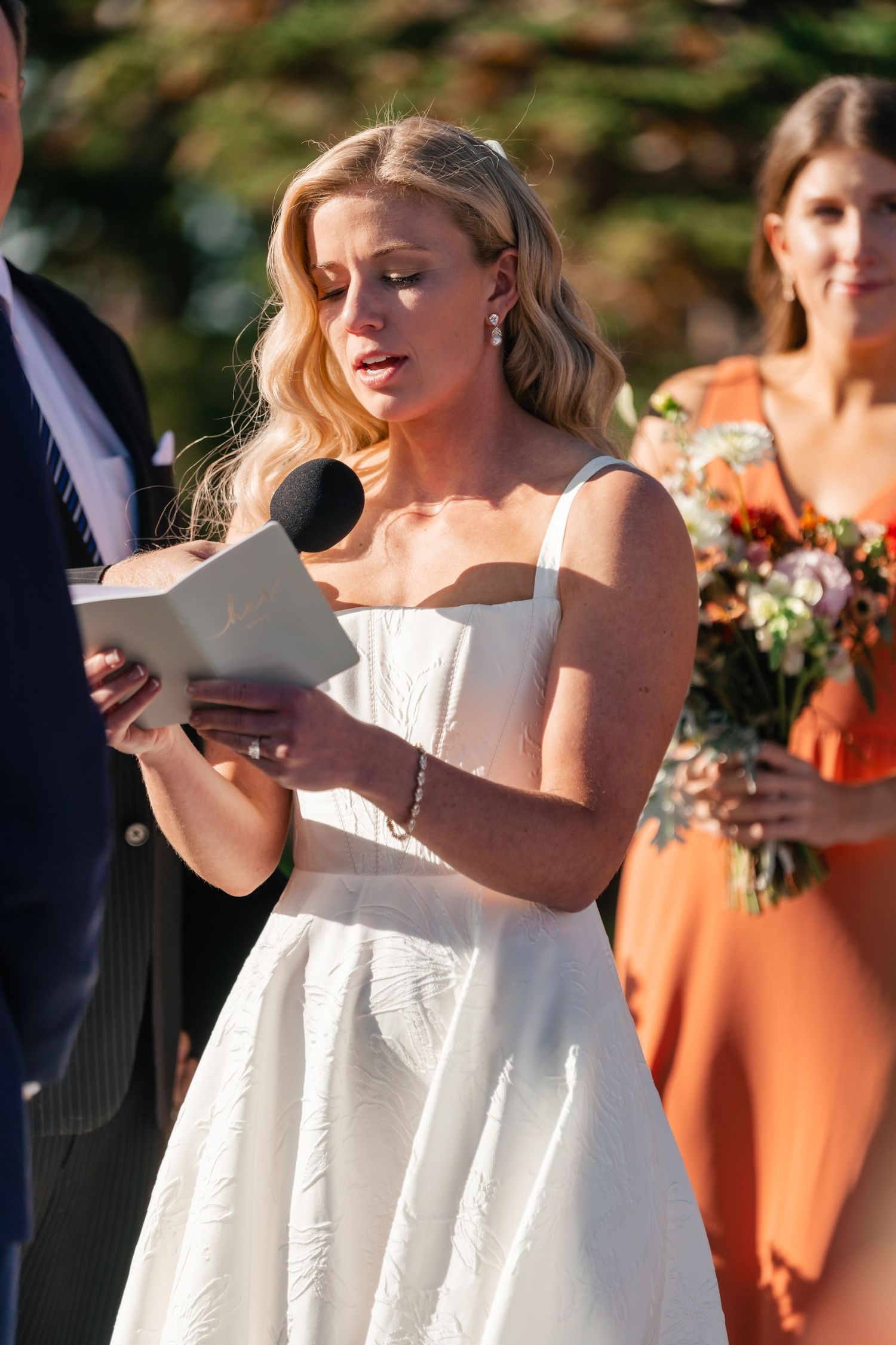 Wedding ceremony attendants hold white booklets while standing outdoors.