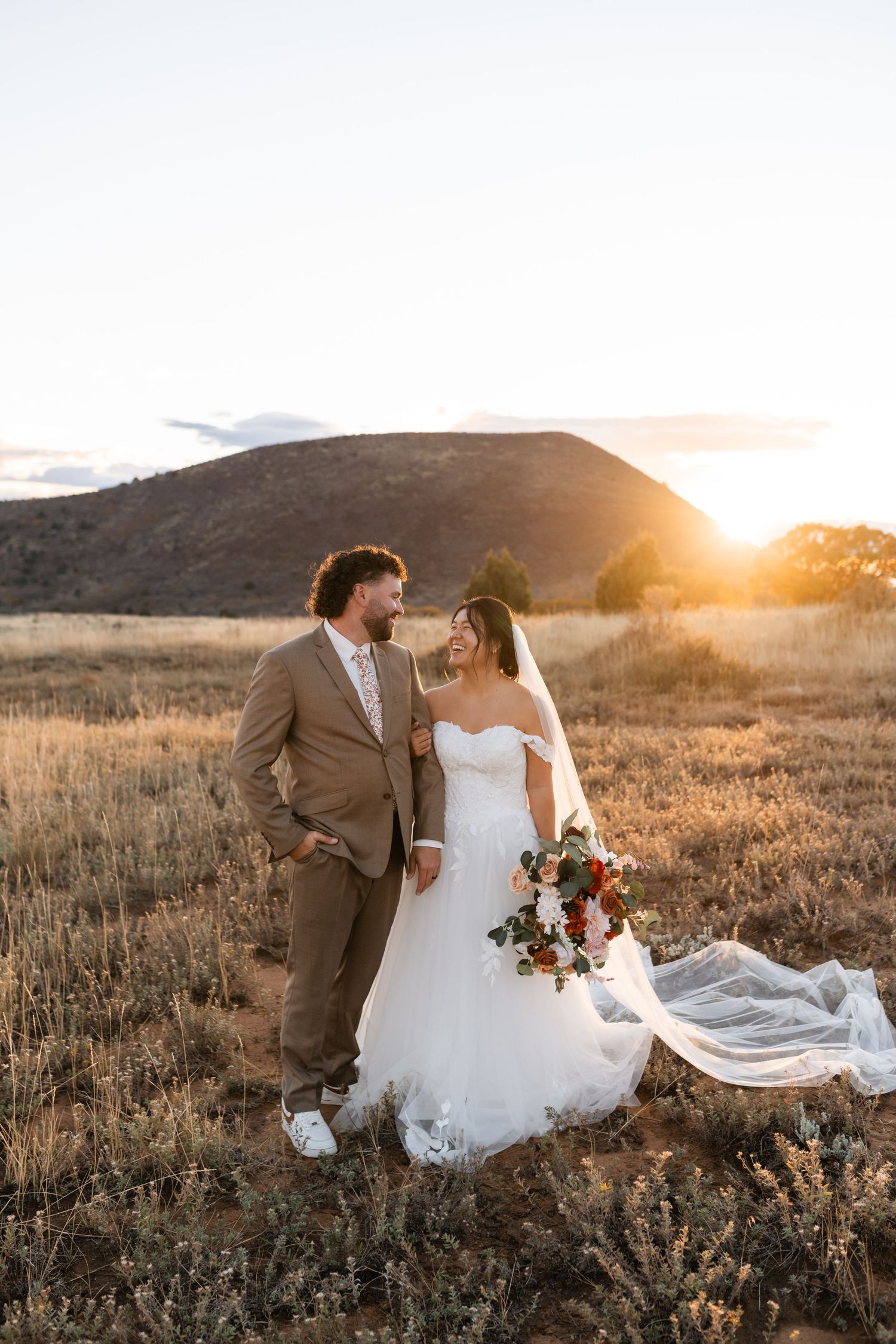 A romantic sunset wedding portrait with flowing dress and mountain scenery.