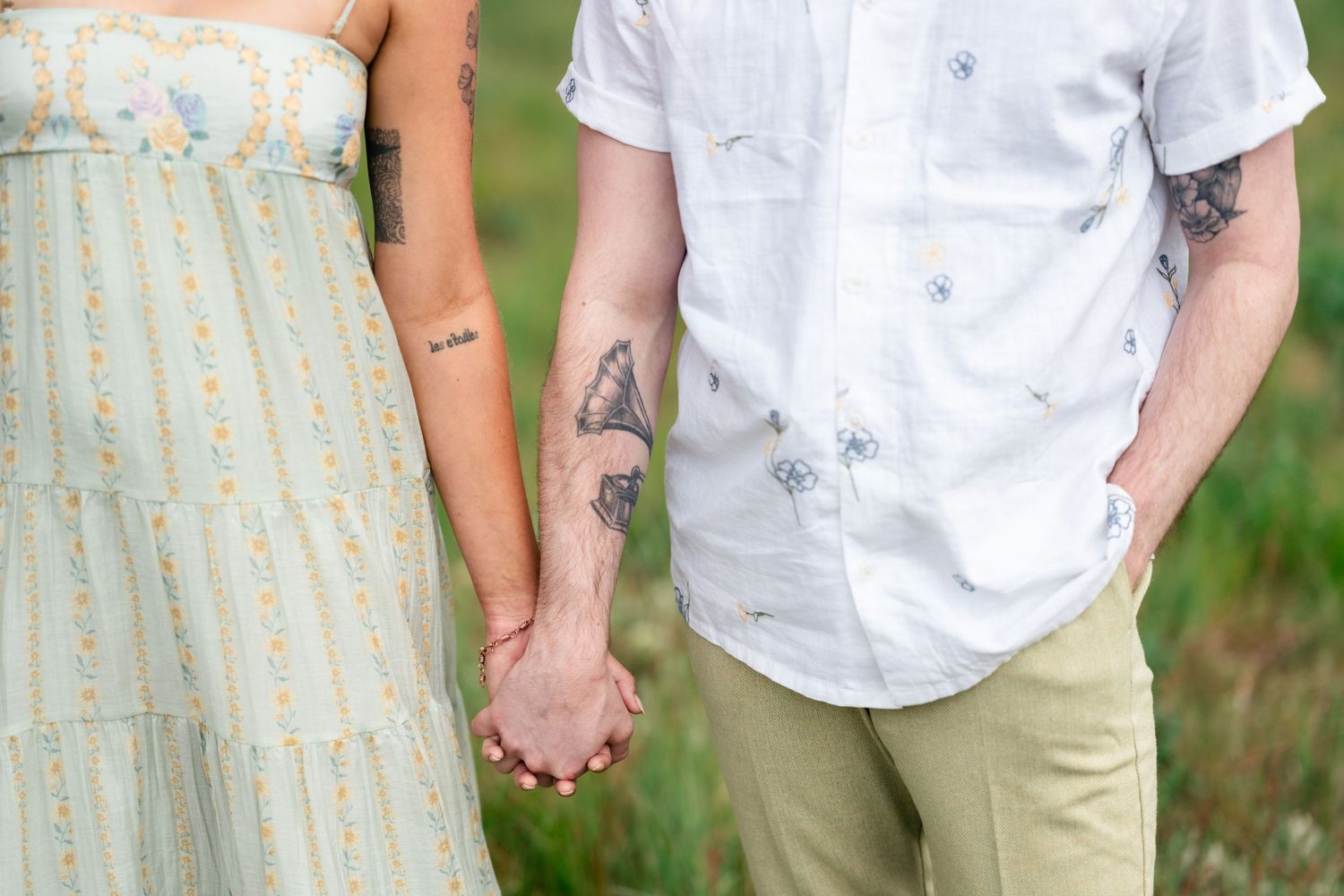 Close-up view of two people holding hands outdoors, wearing casual summer attire.
