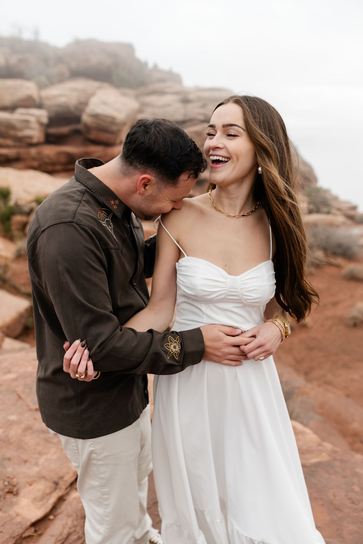 A romantic couple shares intimate moments in white wedding attire against a scenic desert landscape at sunset.