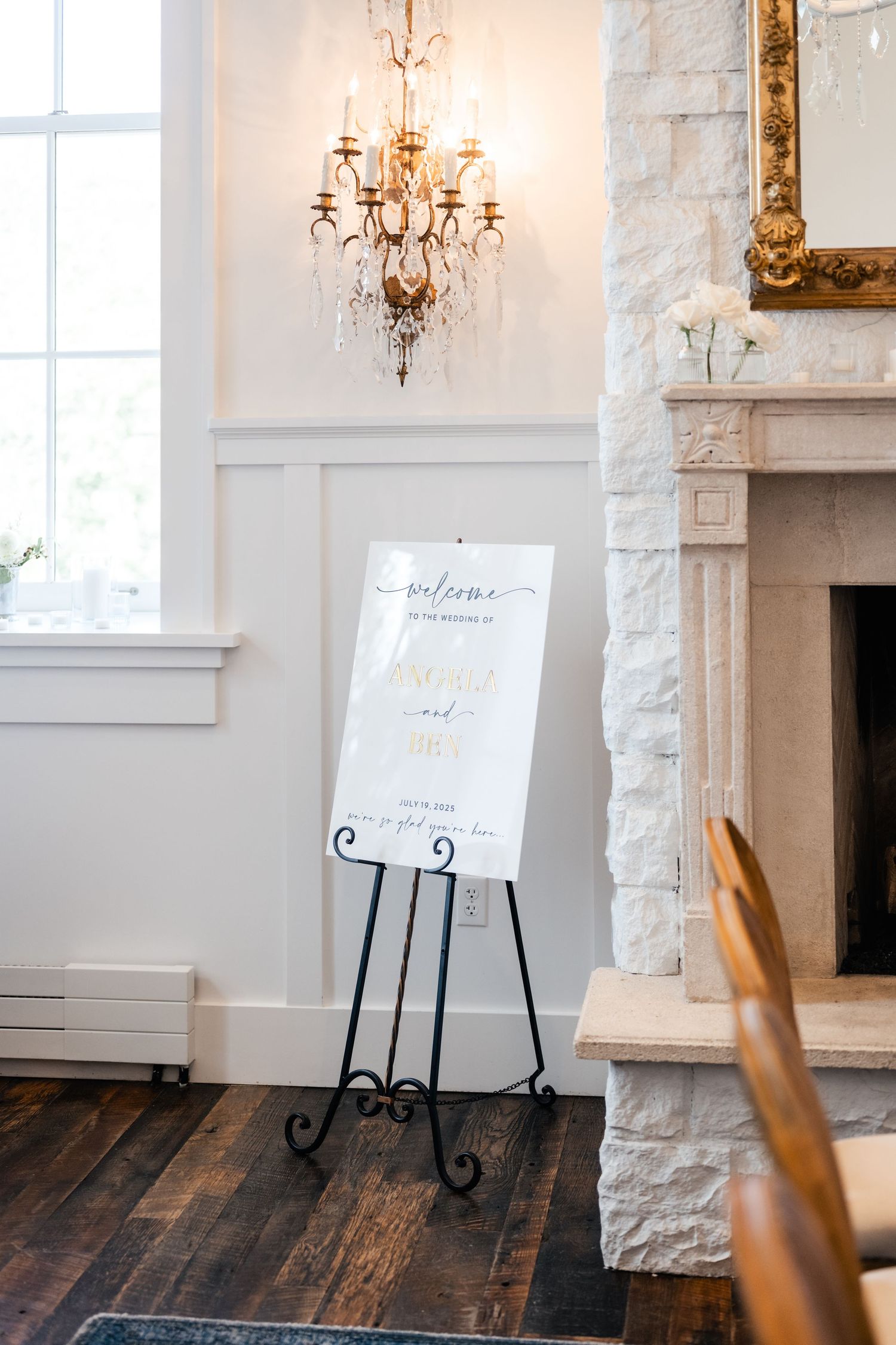 Elegant event space with white stone fireplace, wall sconces, and display easels on rustic wooden floors.