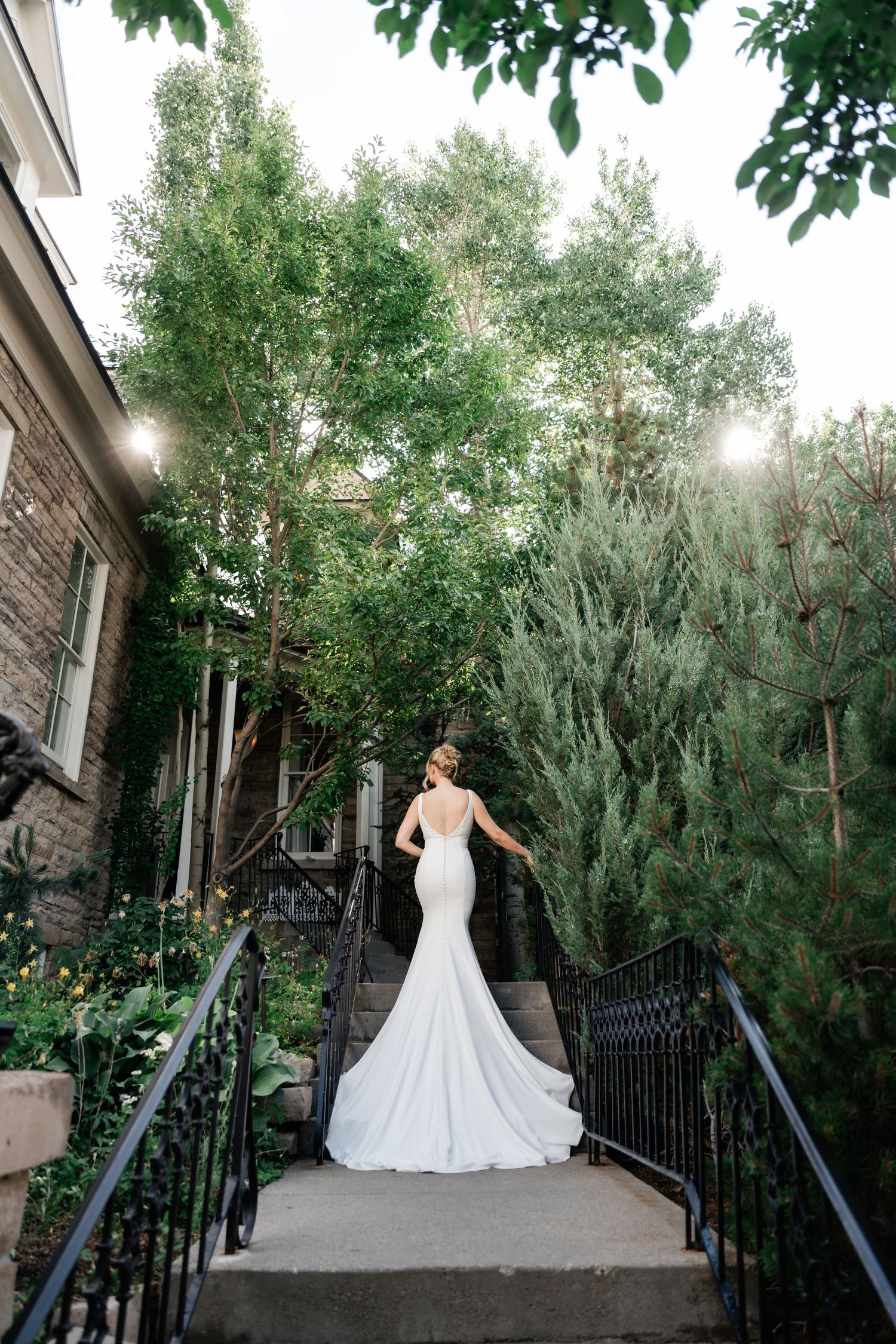 A stunning wedding dress with a long train is showcased on outdoor stone steps surrounded by greenery.