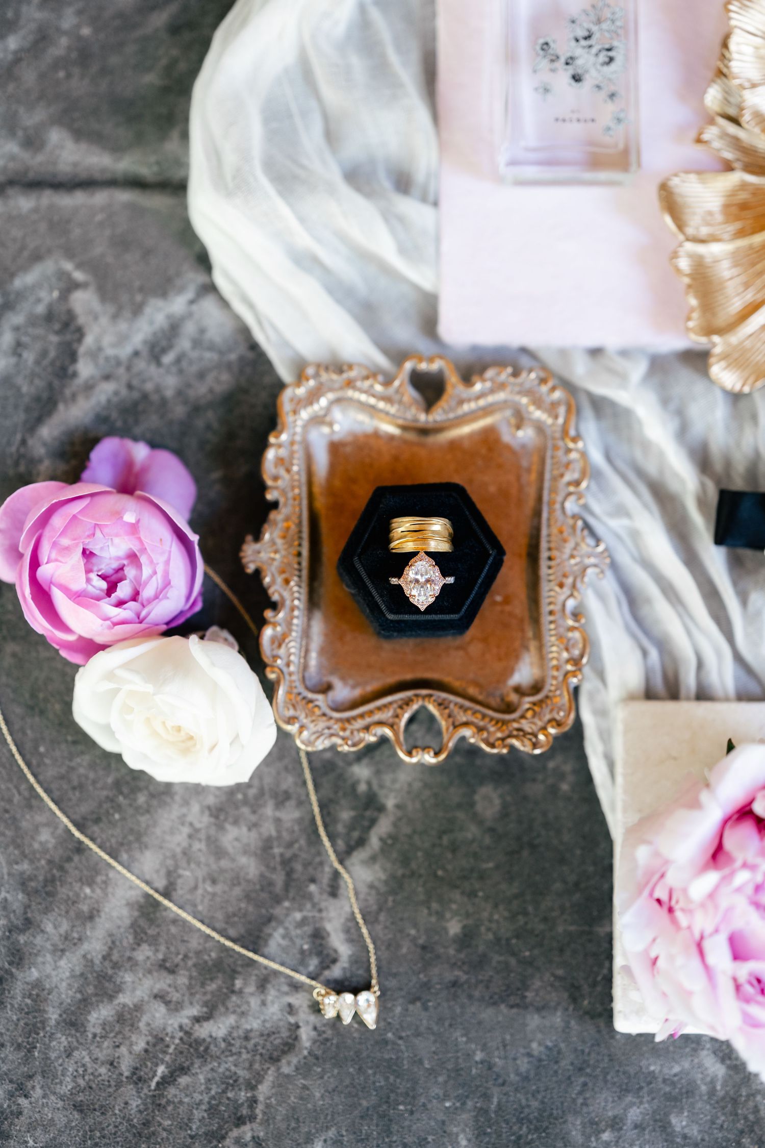 Wedding ring displayed in ornate gold frame with pink and white roses and delicate jewelry.