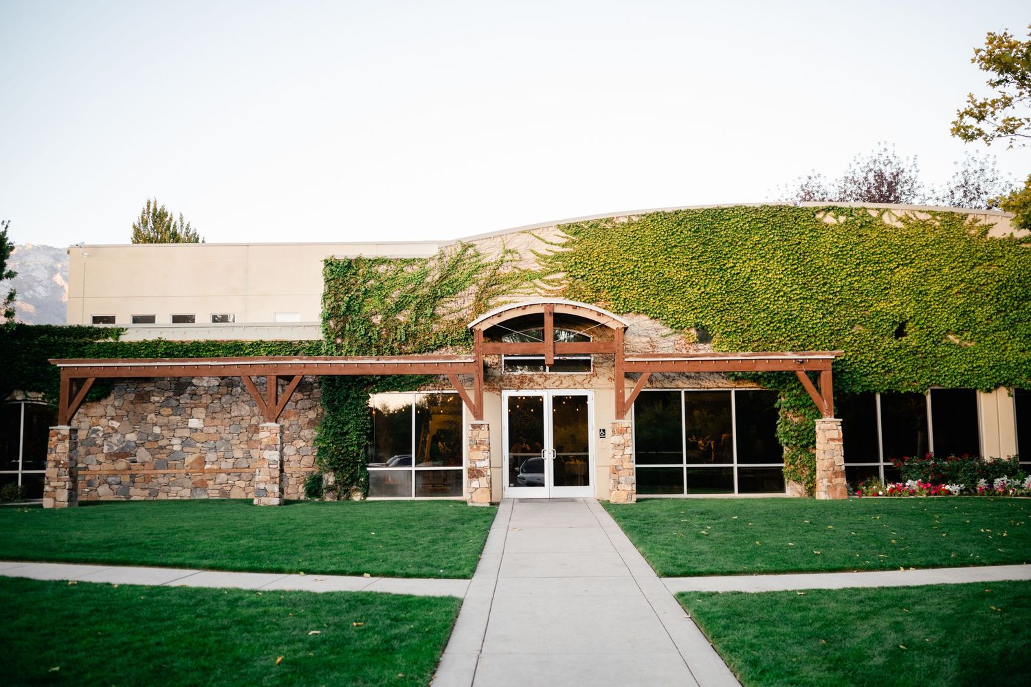 Modern building entrance with stone facade and grass-covered earth roof features glass doors and concrete walkway approach.