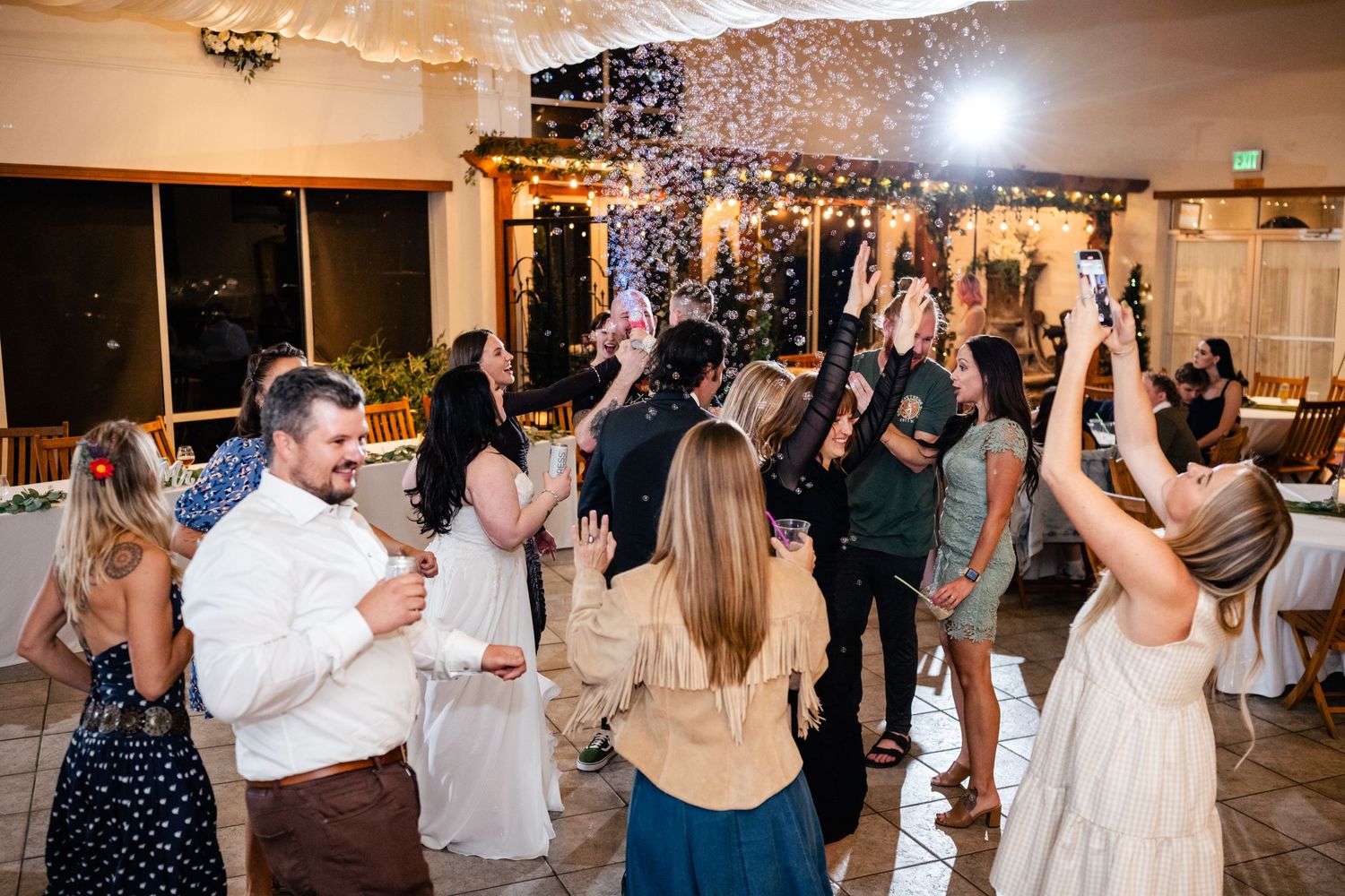 Partygoers dancing enthusiastically under sparkling lights at an indoor wedding reception celebration.