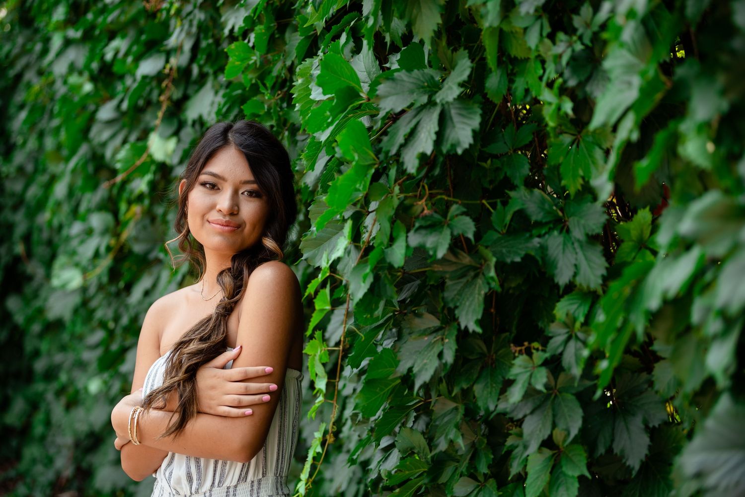 A person poses among lush green grape vines in a vineyard setting during a sunny day.