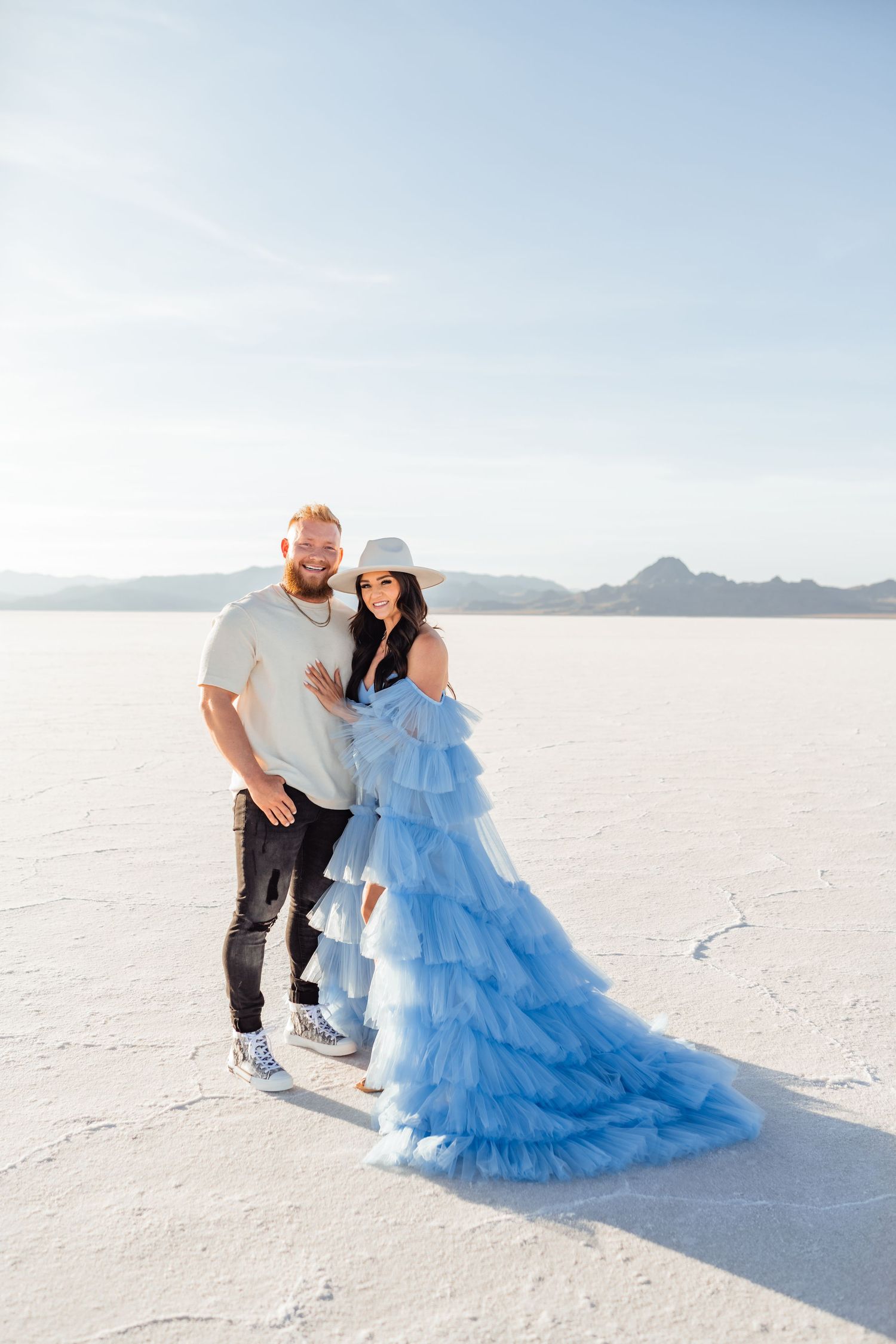 Utah Salt Flats Photographer. Couple poses together on bright white salt flats with woman wearing flowing blue tulle gown.