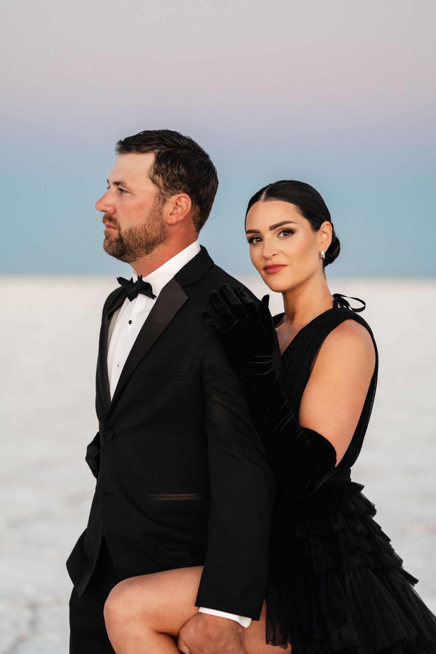 Utah Salt Flats Photos.A couple in formal attire poses intimately against a bright salt flat landscape with mountains in the background.