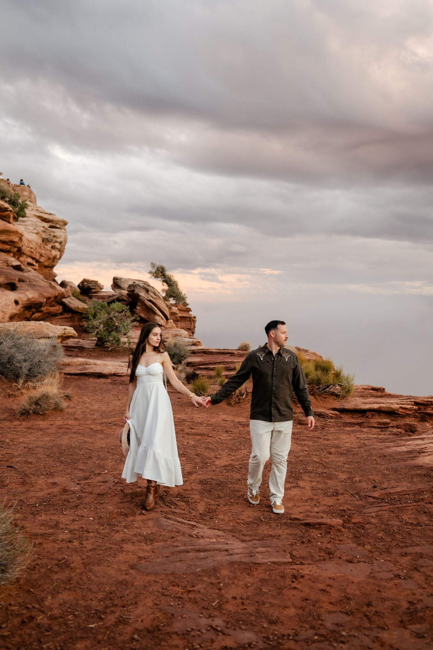 A couple dances together on red rock formations during sunset in a desert landscape.