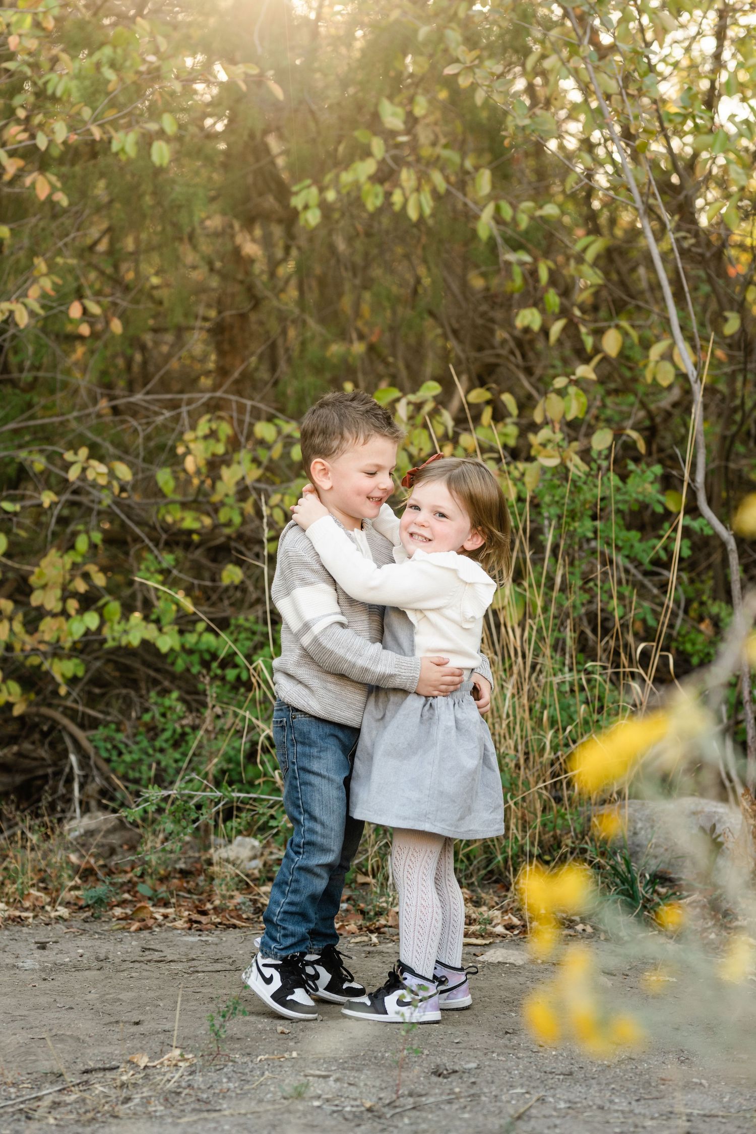Two young children playing and hugging outdoors in front of autumn foliage at sunset.