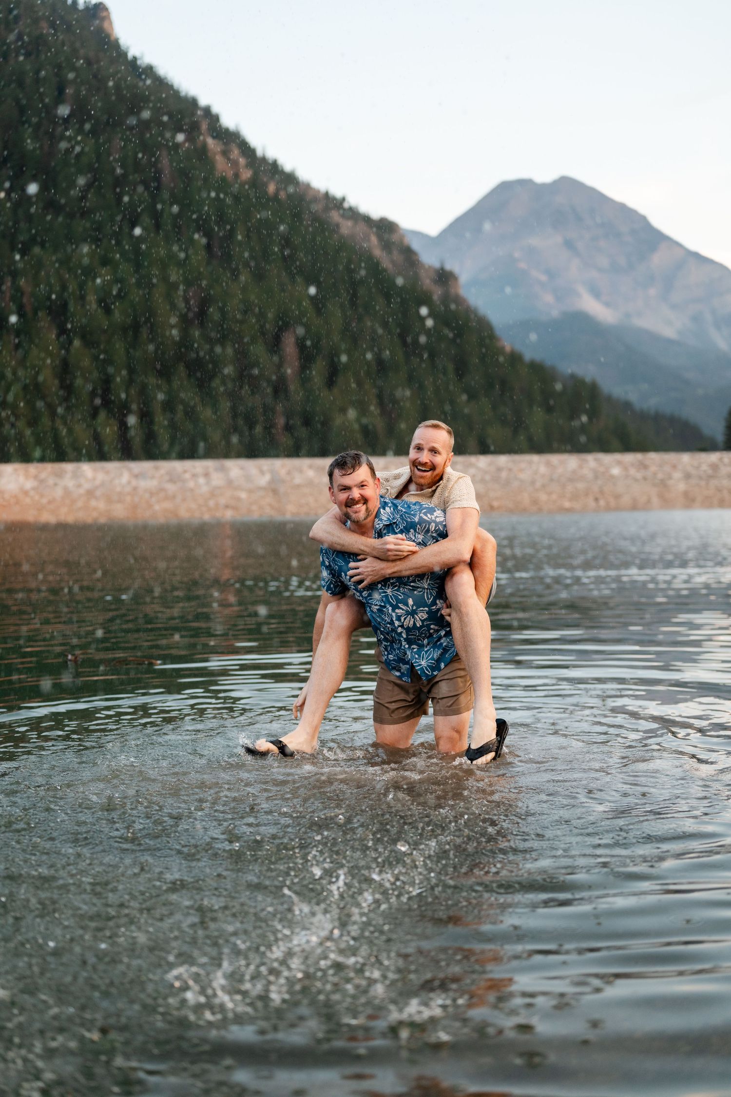 Couple having a water fight at Tibble Fork Reservoir. A man gives his partner a piggyback ride while wading through a scenic mountain lake.