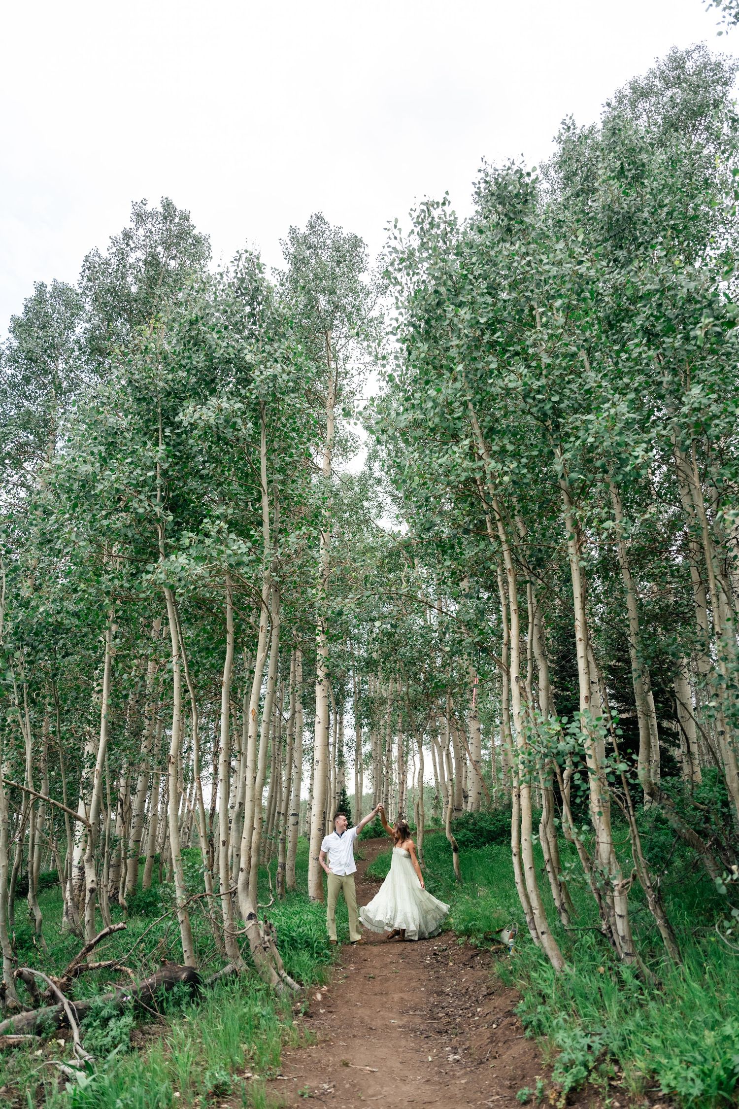 A couple walks down a winding dirt path through a serene aspen forest.