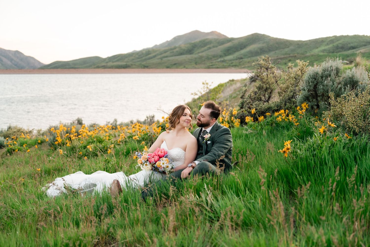 Newlyweds share romantic moments among yellow wildflowers with mountain vistas and a lake.