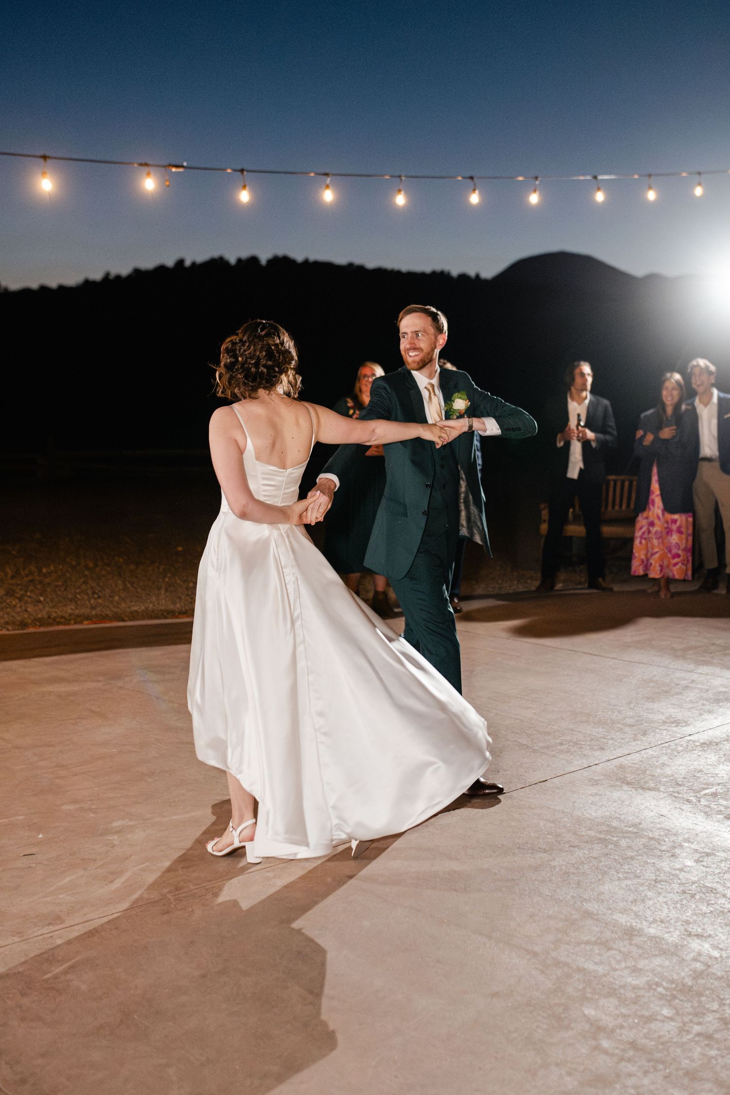 A couple dances under string lights during their evening wedding reception.