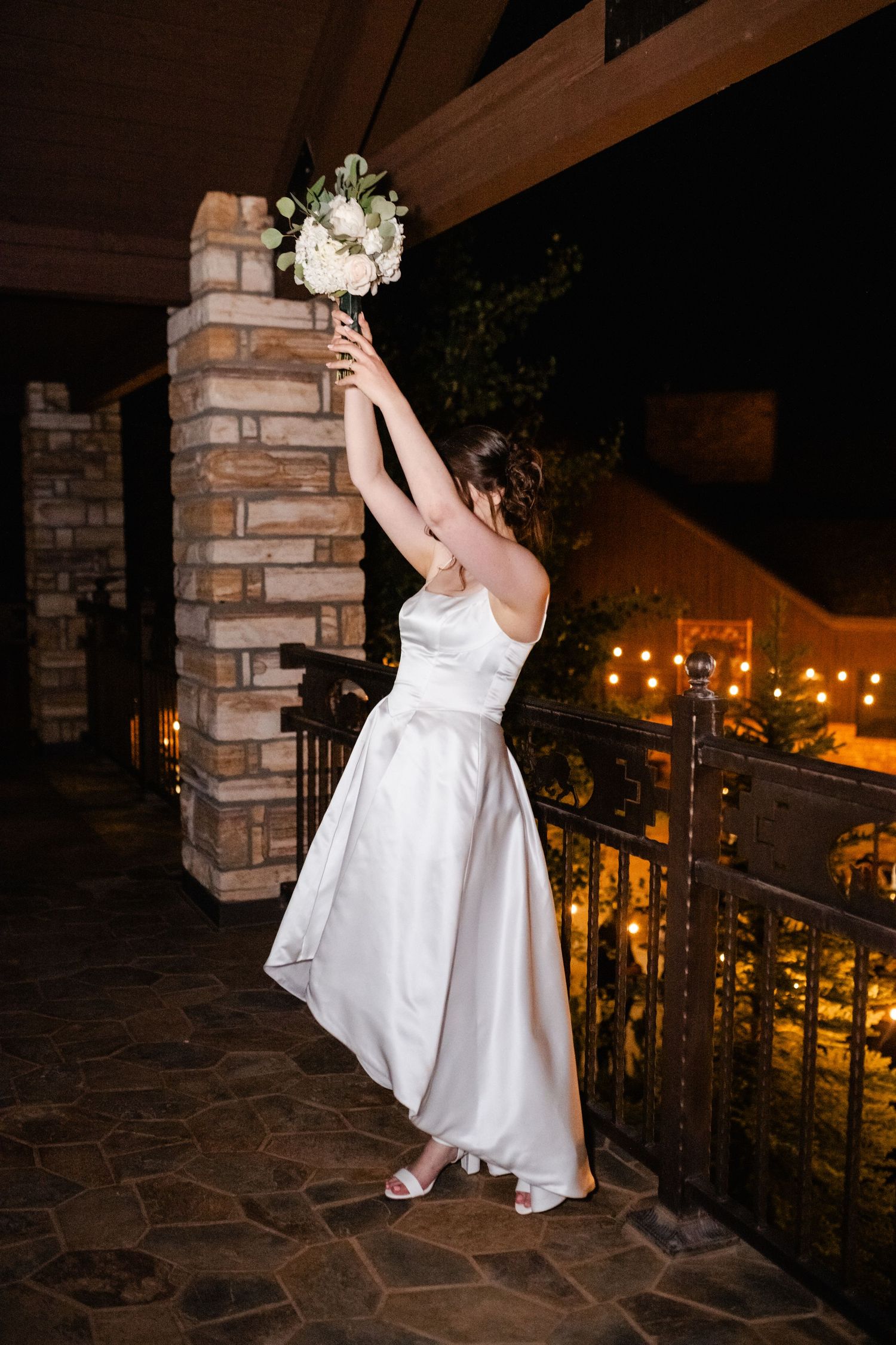 Elegant bridal photos on a stone balcony at night with city lights in background.