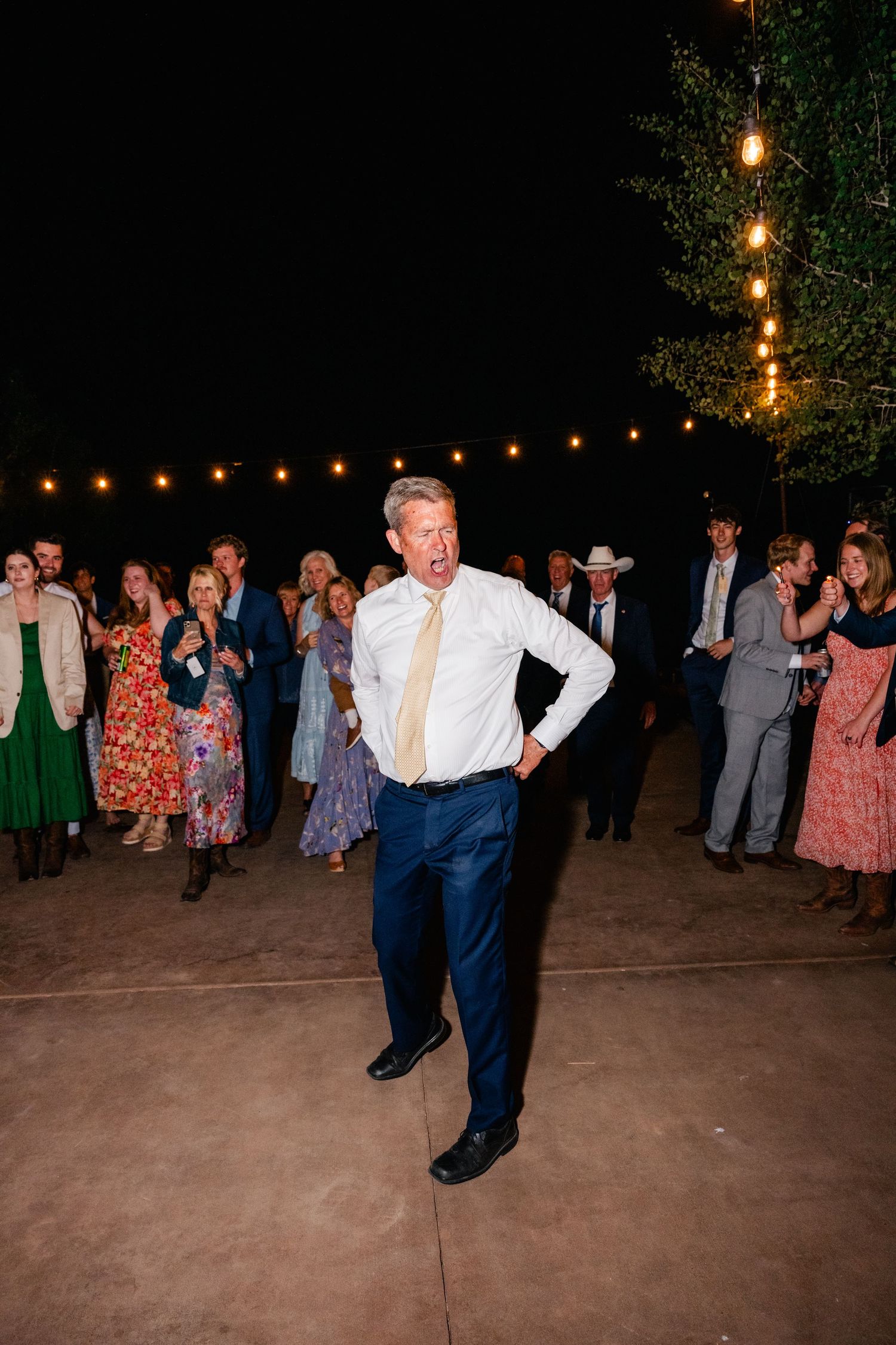 Wedding guests dance on an outdoor patio under string lights at night.