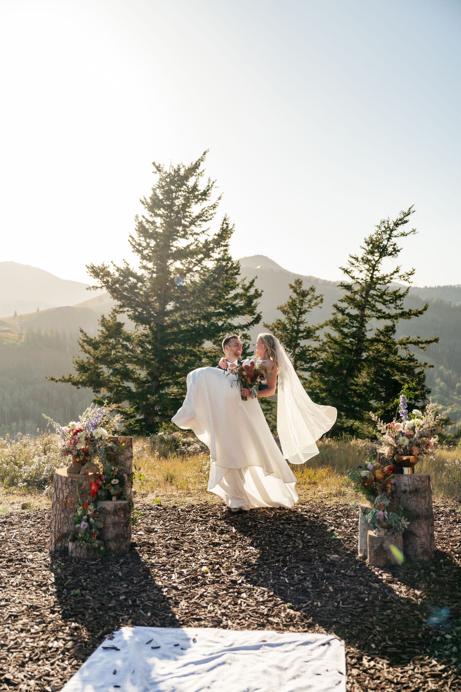 A white wedding aisle runner contrasts against rocky terrain with mountain vistas and pine trees.