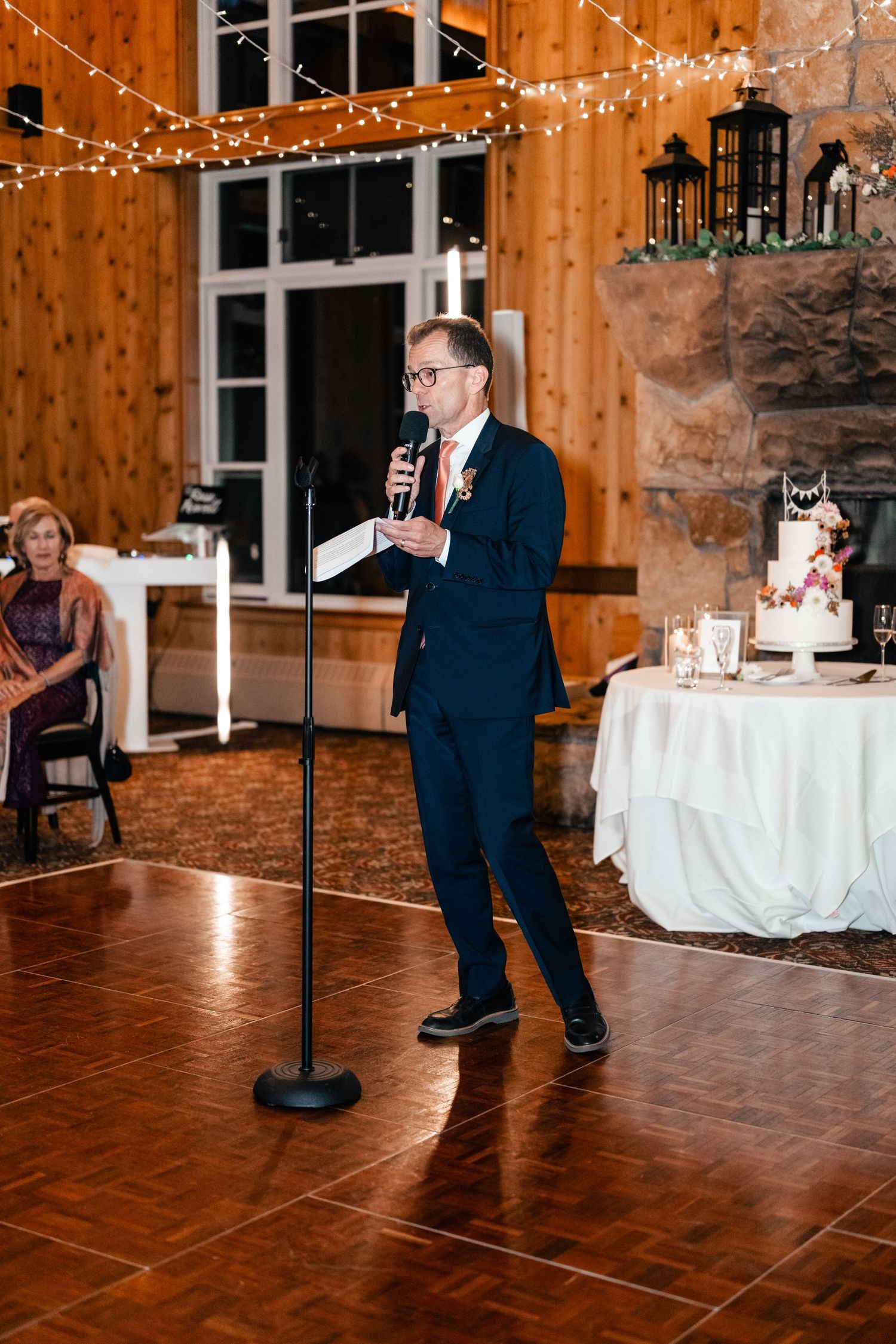 Wedding reception dance in a rustic wooden venue decorated with string lights.