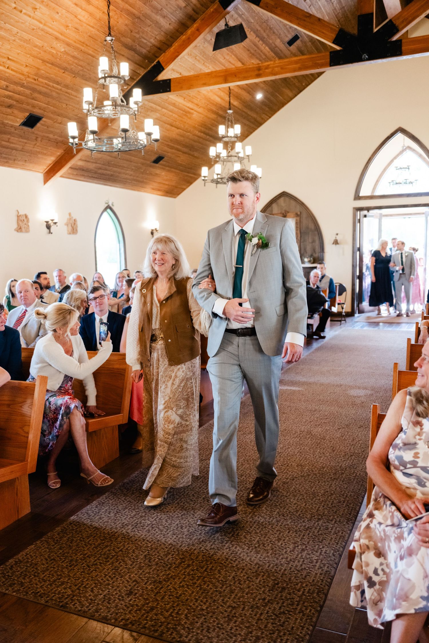 Wedding guests dancing and mingling in a rustic church reception hall with wooden beams and chandeliers.