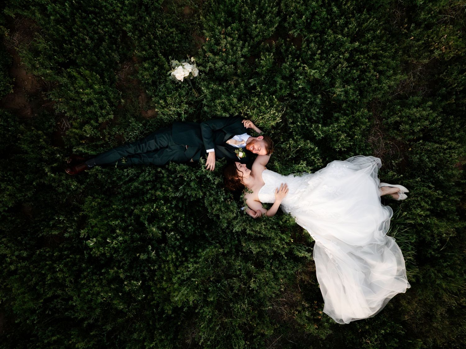 A couple shares a romantic kiss while dancing together in a lush garden setting during their wedding celebration.